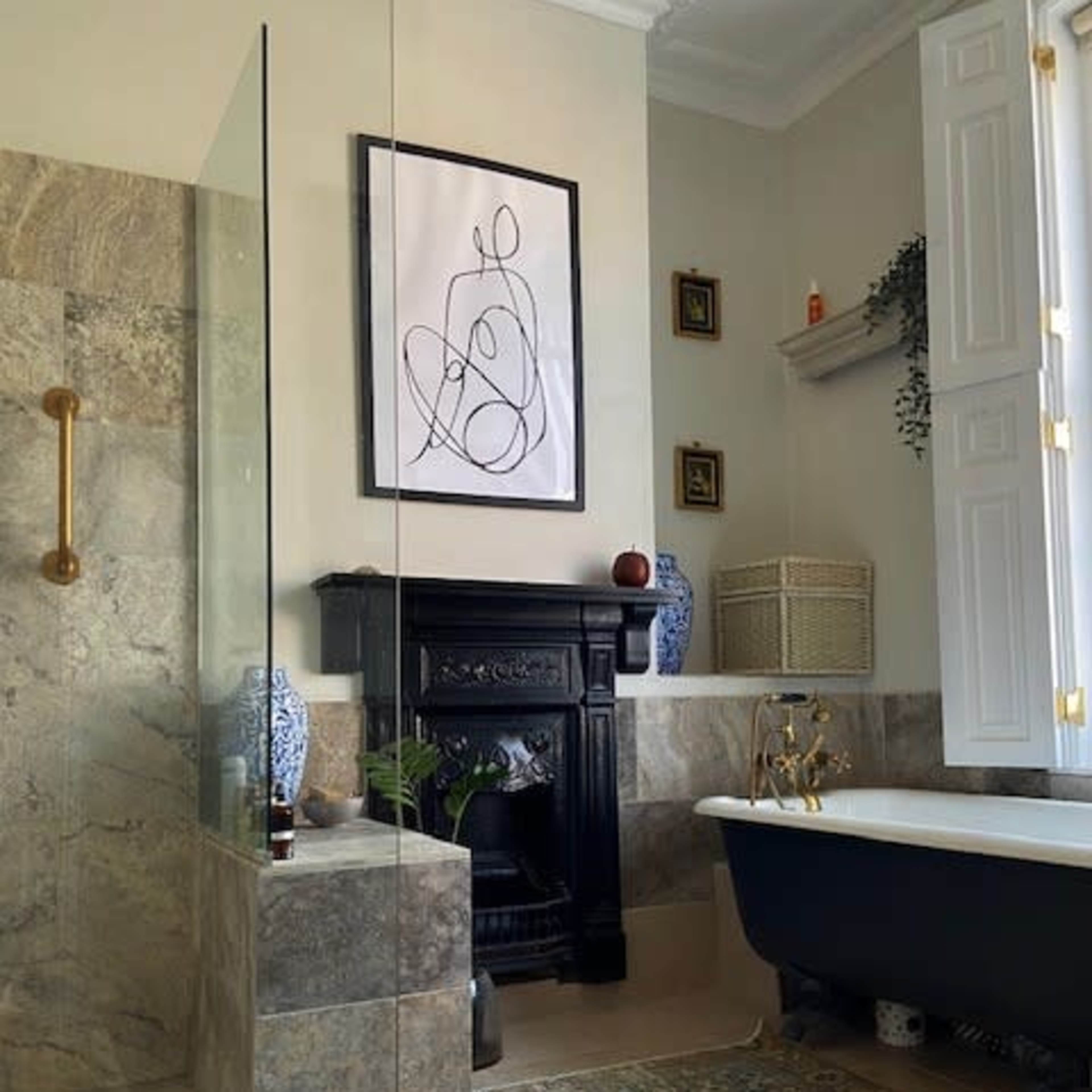A bathroom featuring a freestanding bathtub, a glass shower enclosure, and a decorative fireplace, with artwork and storage baskets arranged on the walls and shelves.