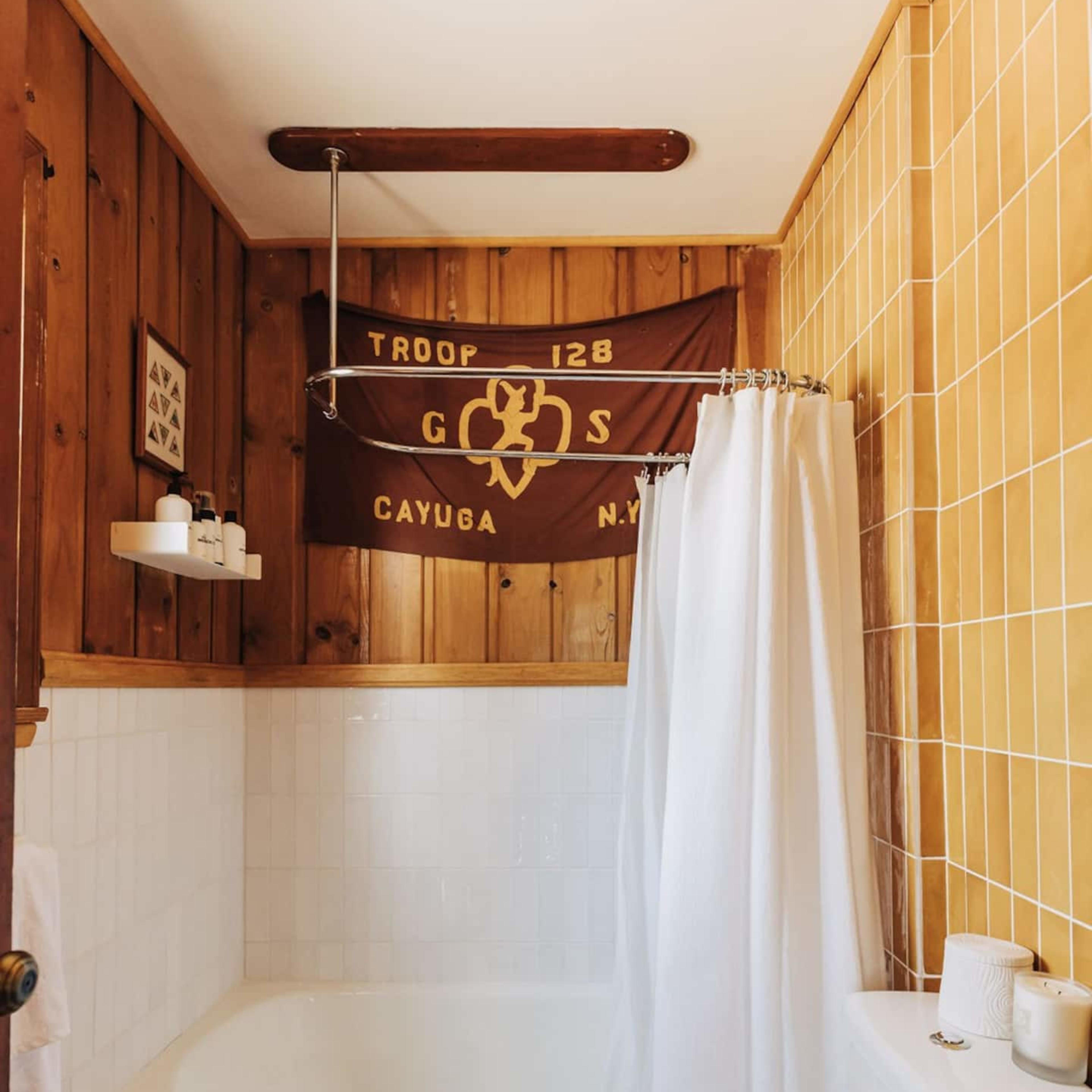A bathroom featuring a shower-tub combination, a toilet, and wooden paneling, with a flag hanging on the wall.