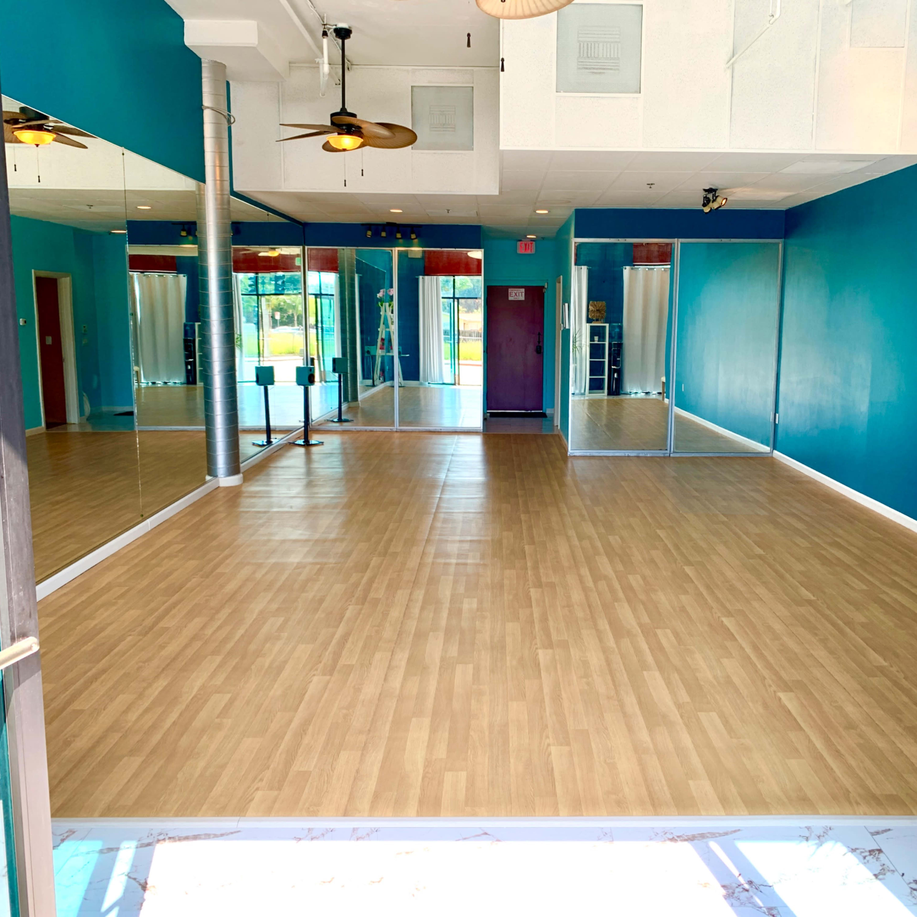 A spacious room with wooden flooring, teal walls, and large mirrors on one side.