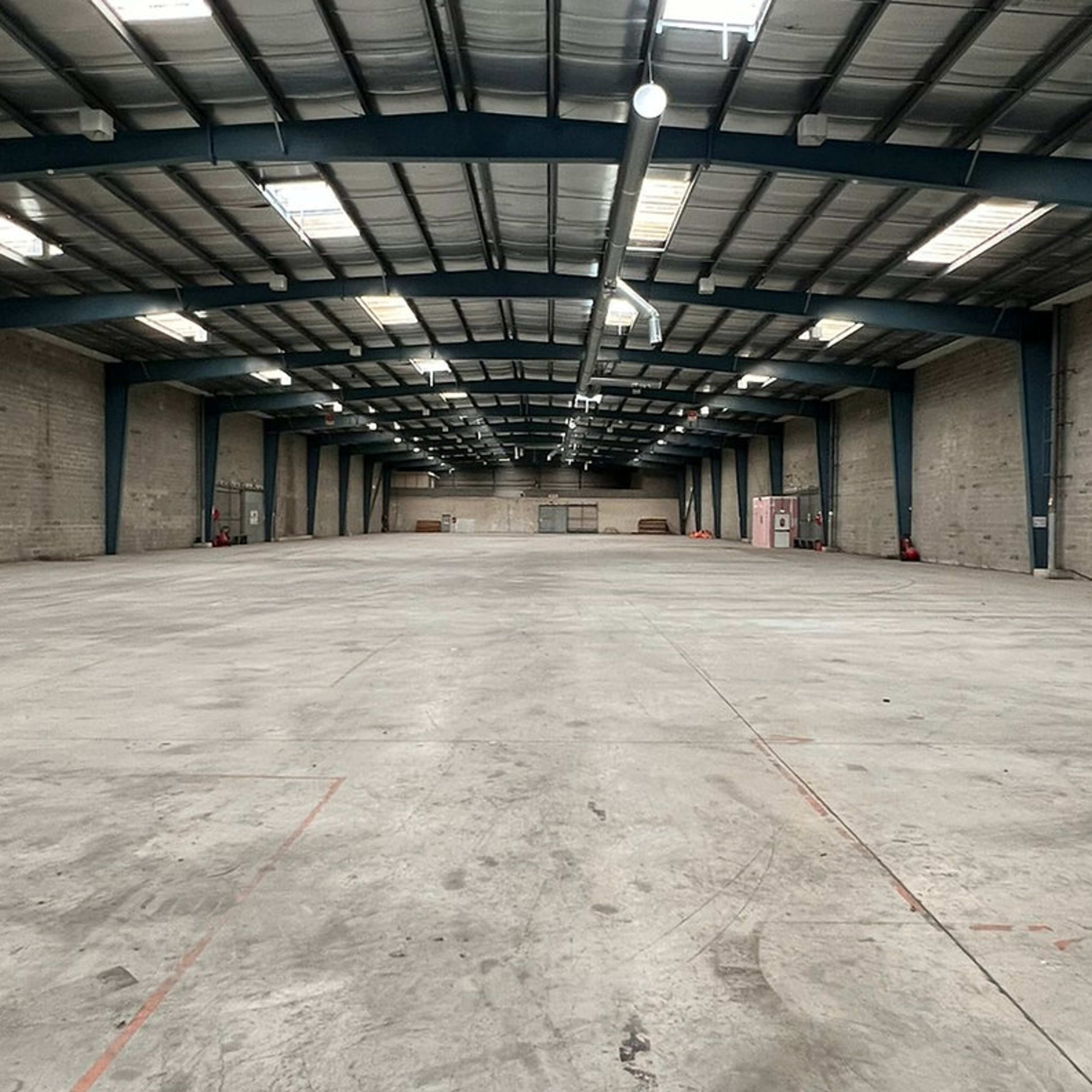 A large, empty industrial warehouse with concrete floors and high metal ceilings.