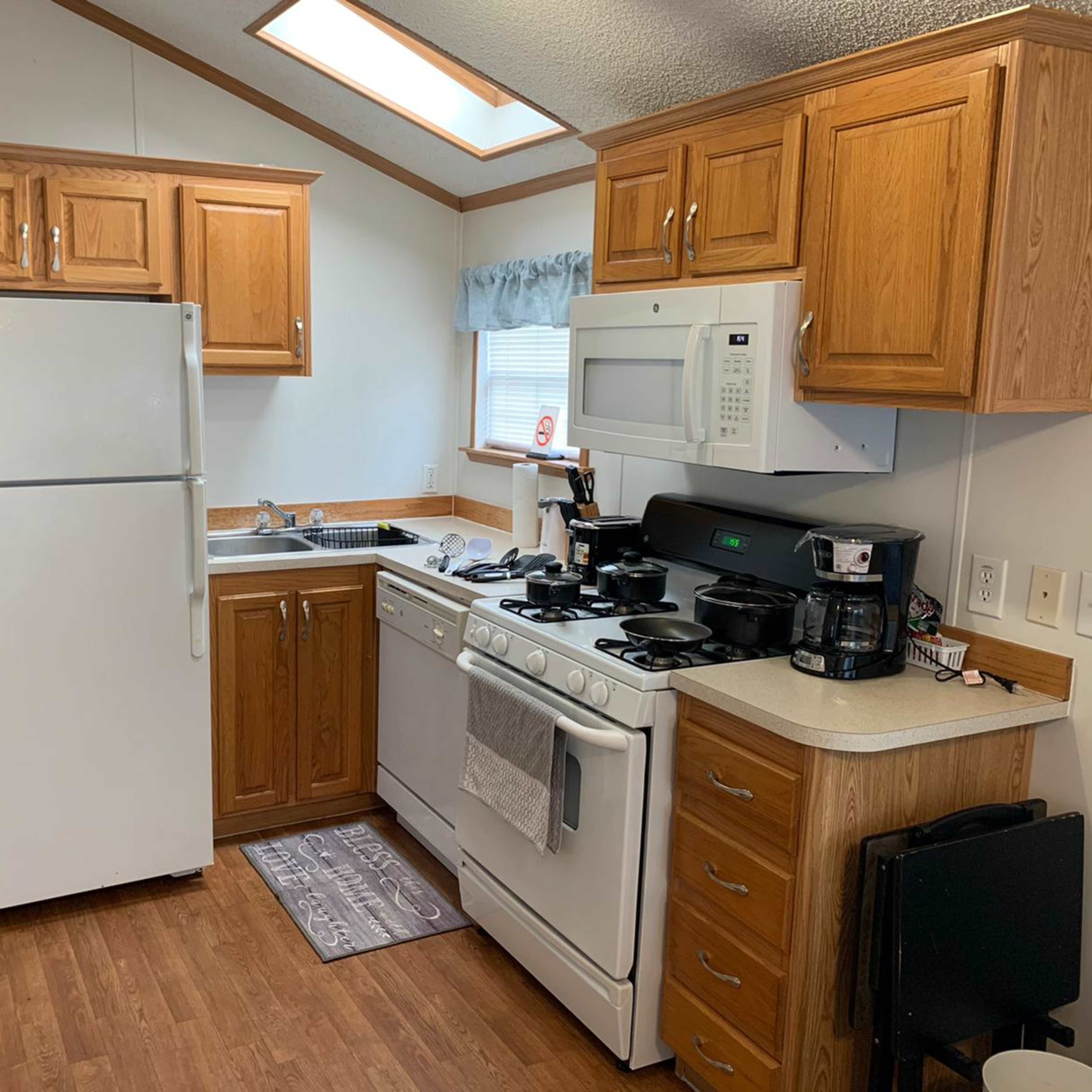 A compact kitchen featuring wooden cabinets, a white refrigerator, a gas stove, and a sink with kitchen appliances on the countertop.