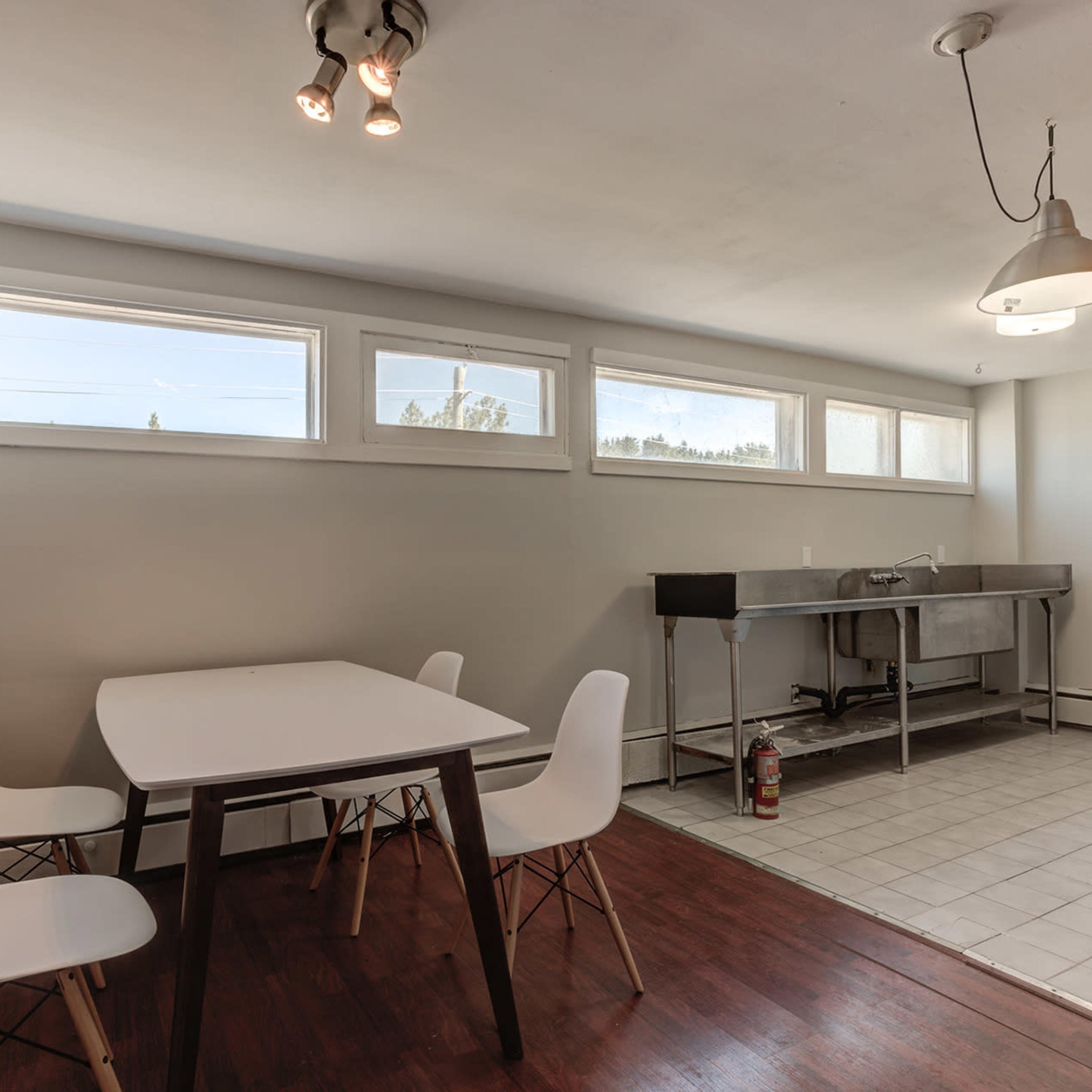 A small dining area features a white table and four chairs, with a long sink and large windows along one wall.