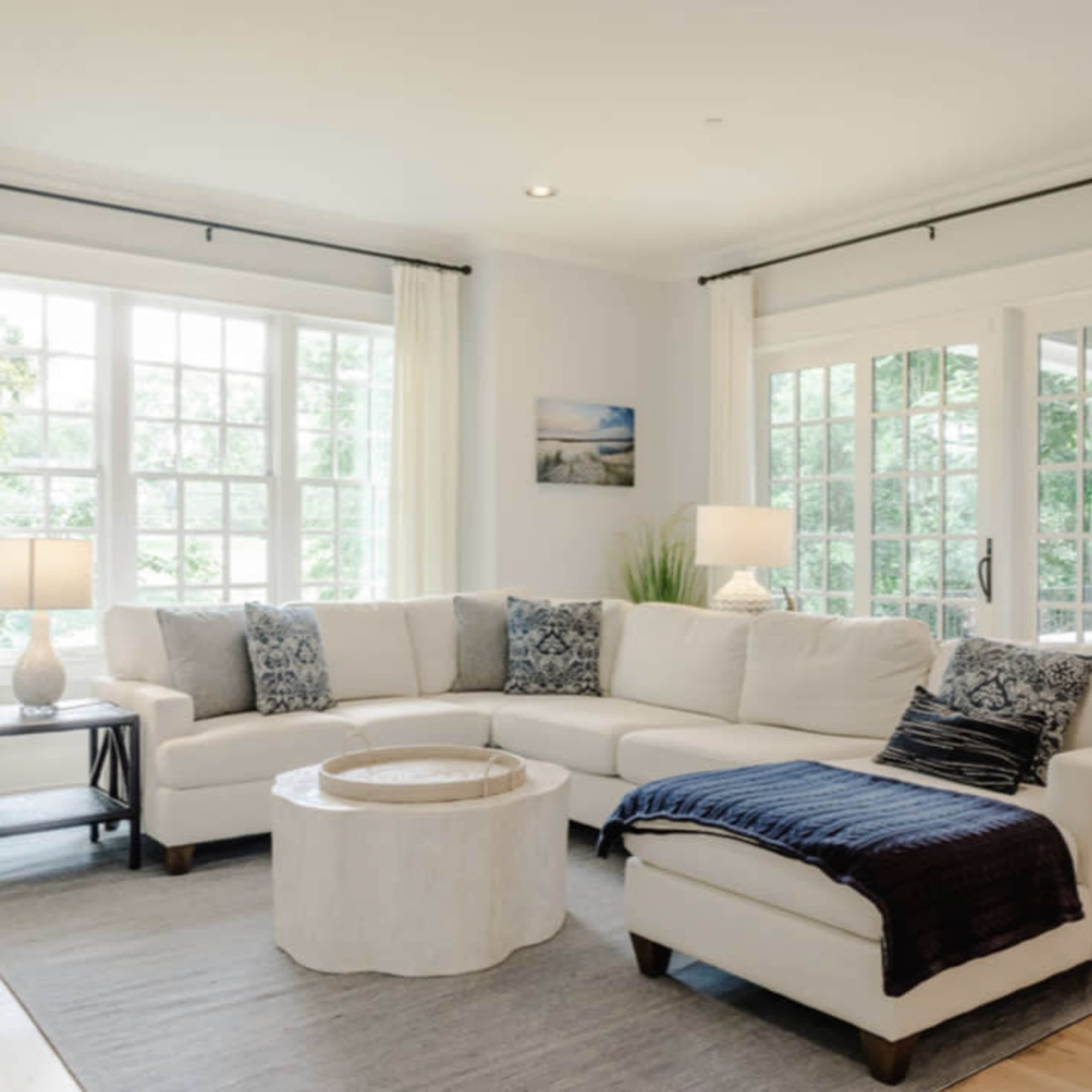 A bright living room featuring a large white sectional sofa, a circular coffee table, and large windows with natural light.