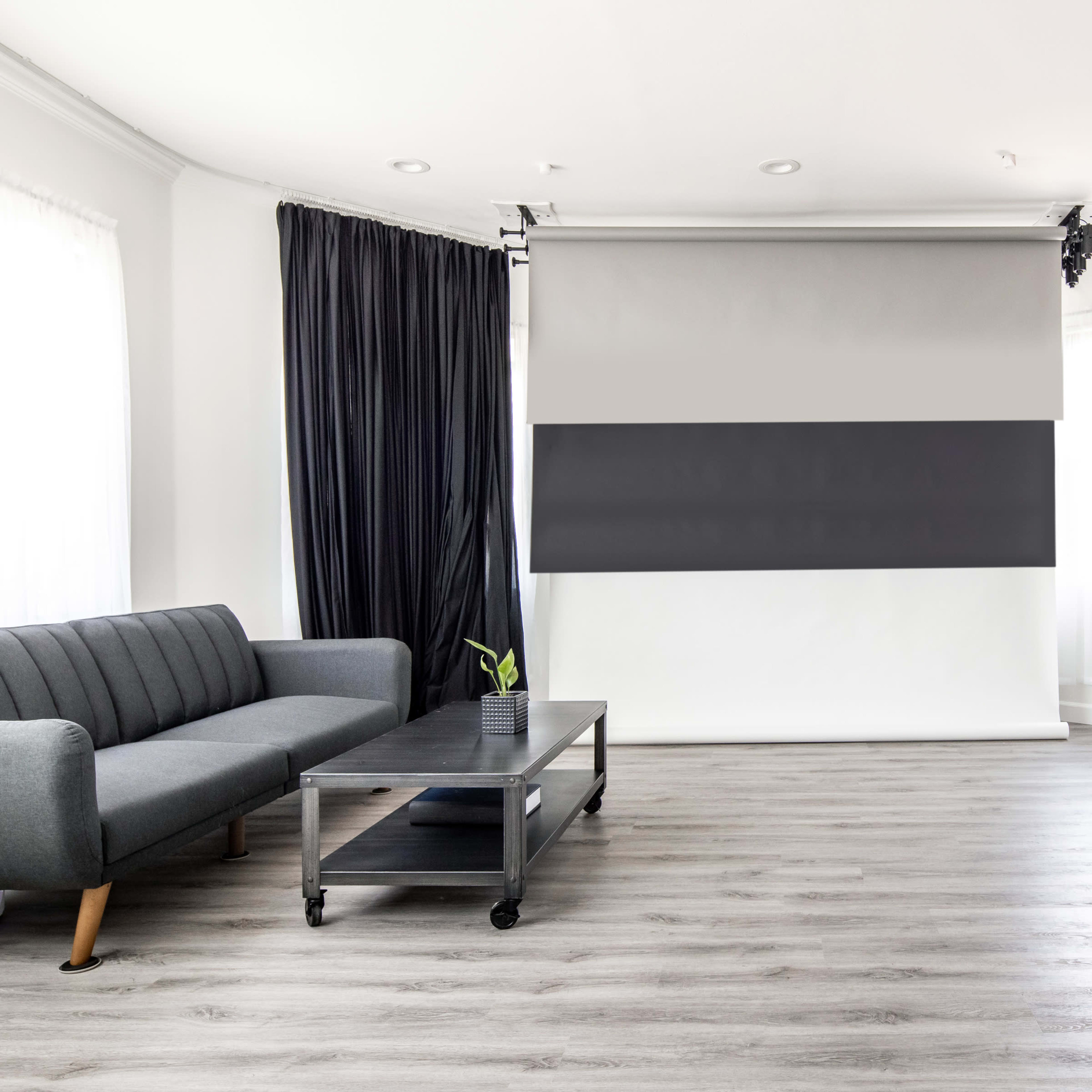A modern living space featuring a gray sofa, a coffee table on wheels, and a photography backdrop setup with black and white panels.