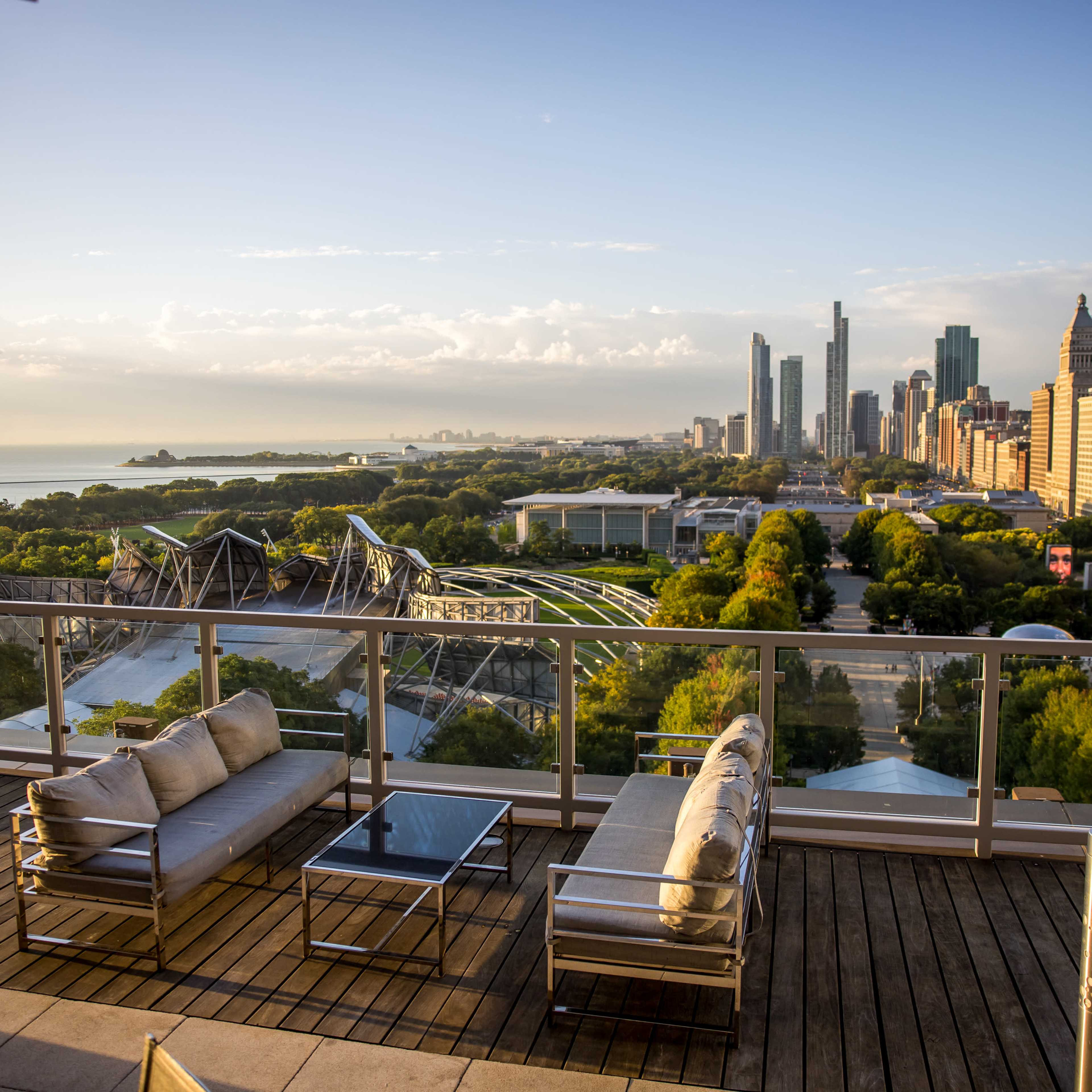 A rooftop view overlooking a city skyline with modern buildings, a park, and Lake Michigan in the distance.
