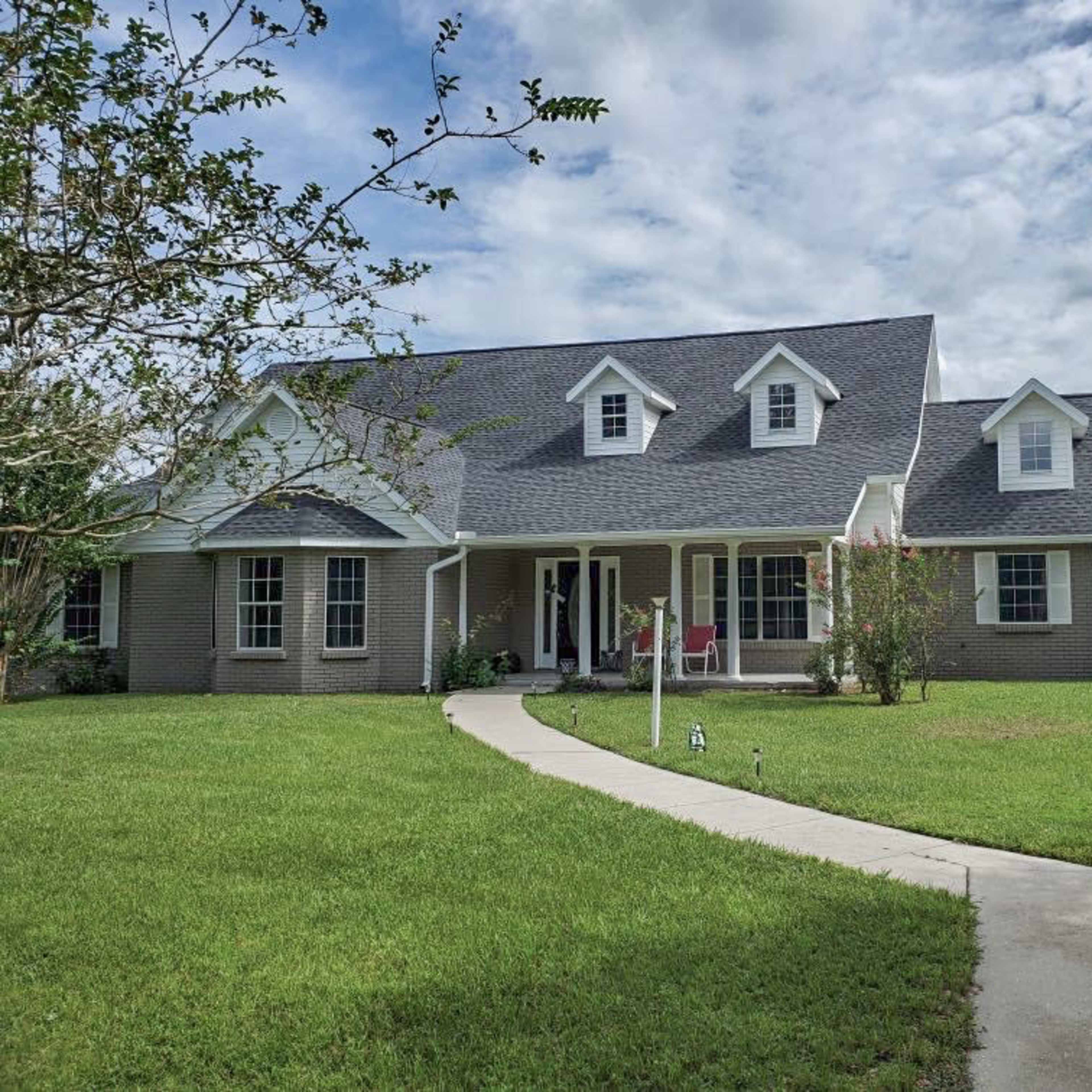 A large, two-story house with a gray roof and porch sits on a well-maintained lawn.