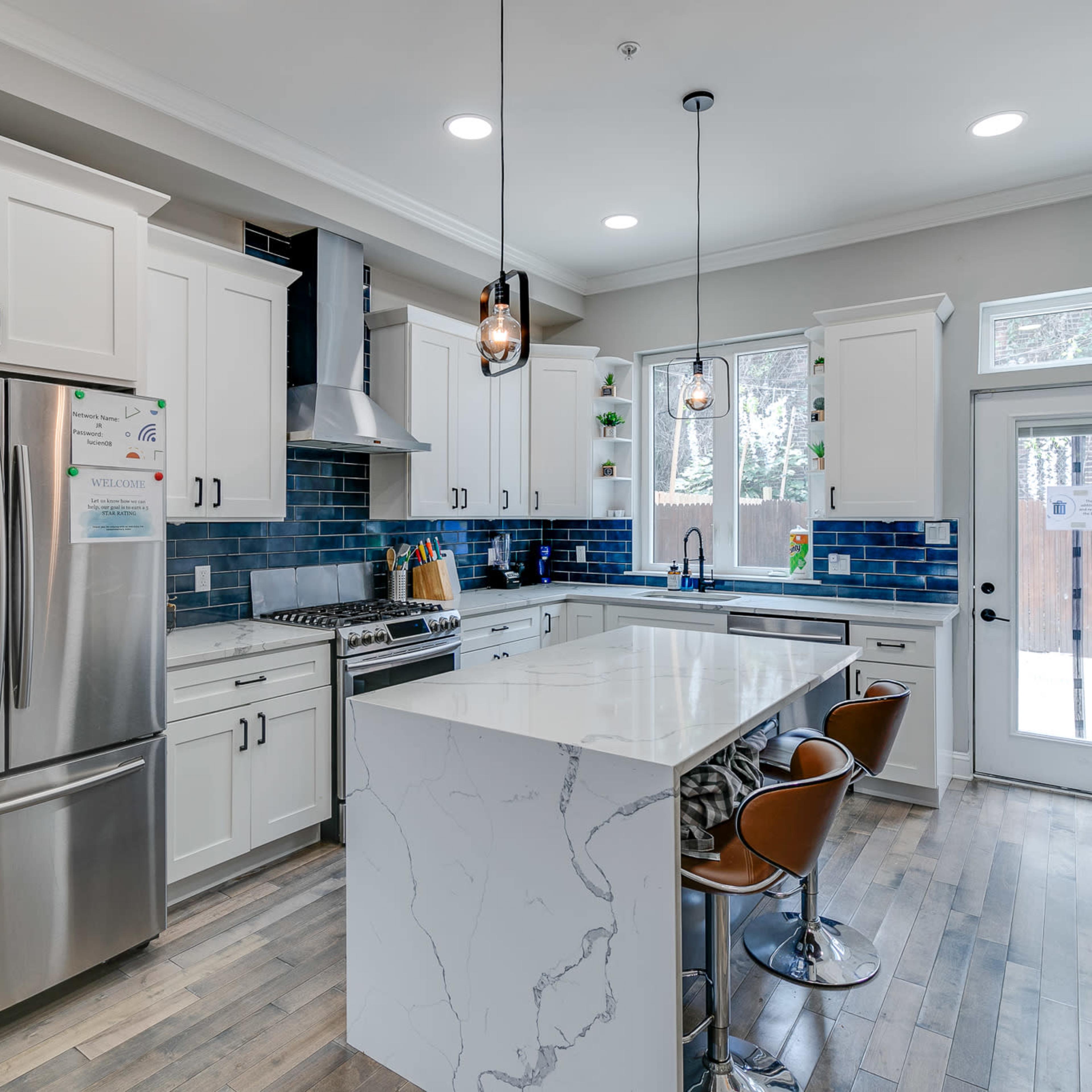 The kitchen features white cabinetry, a large island with a marble countertop, stainless steel appliances, and blue tile backsplash.
