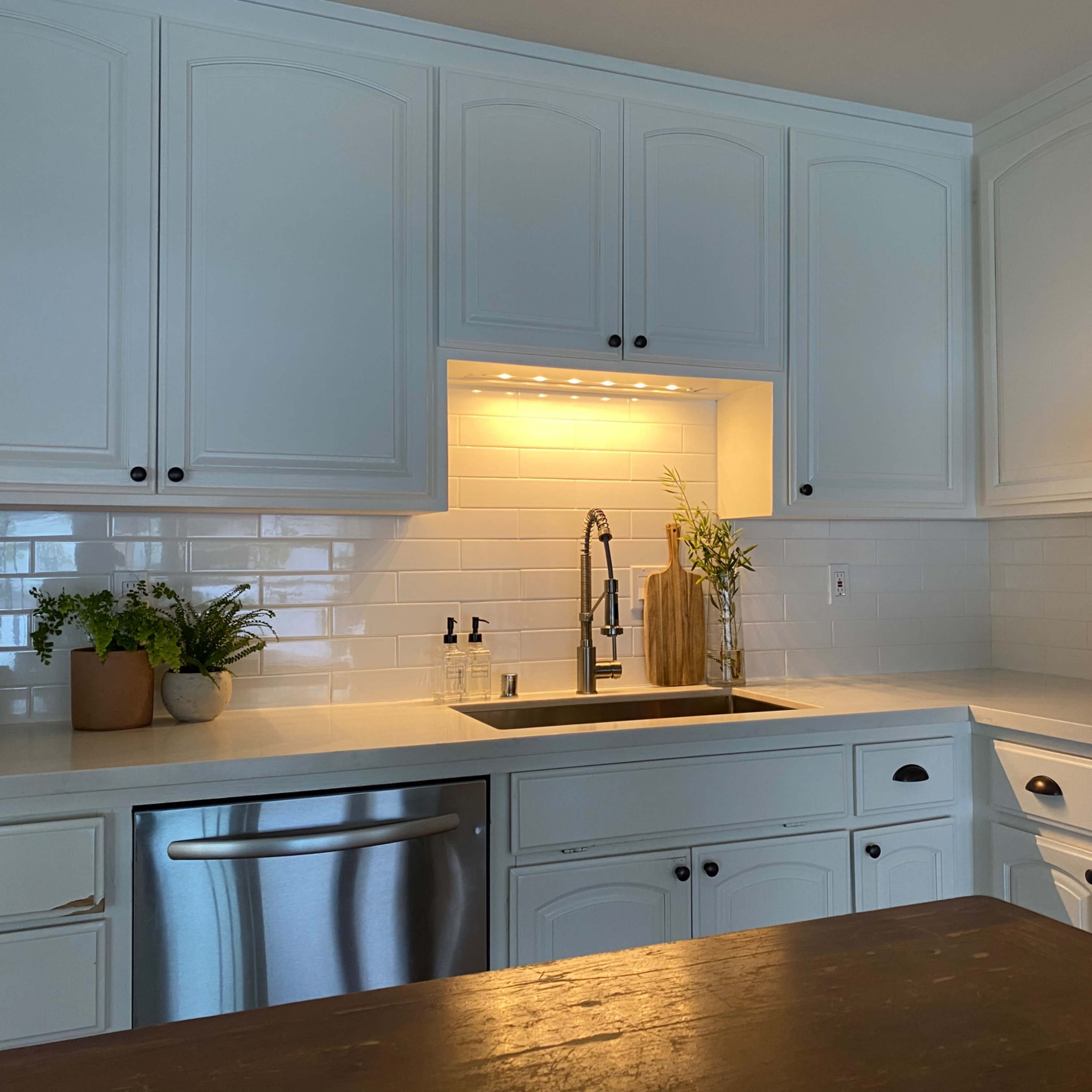 A modern kitchen features white cabinetry, a stainless steel sink, and a backsplash of white subway tiles.