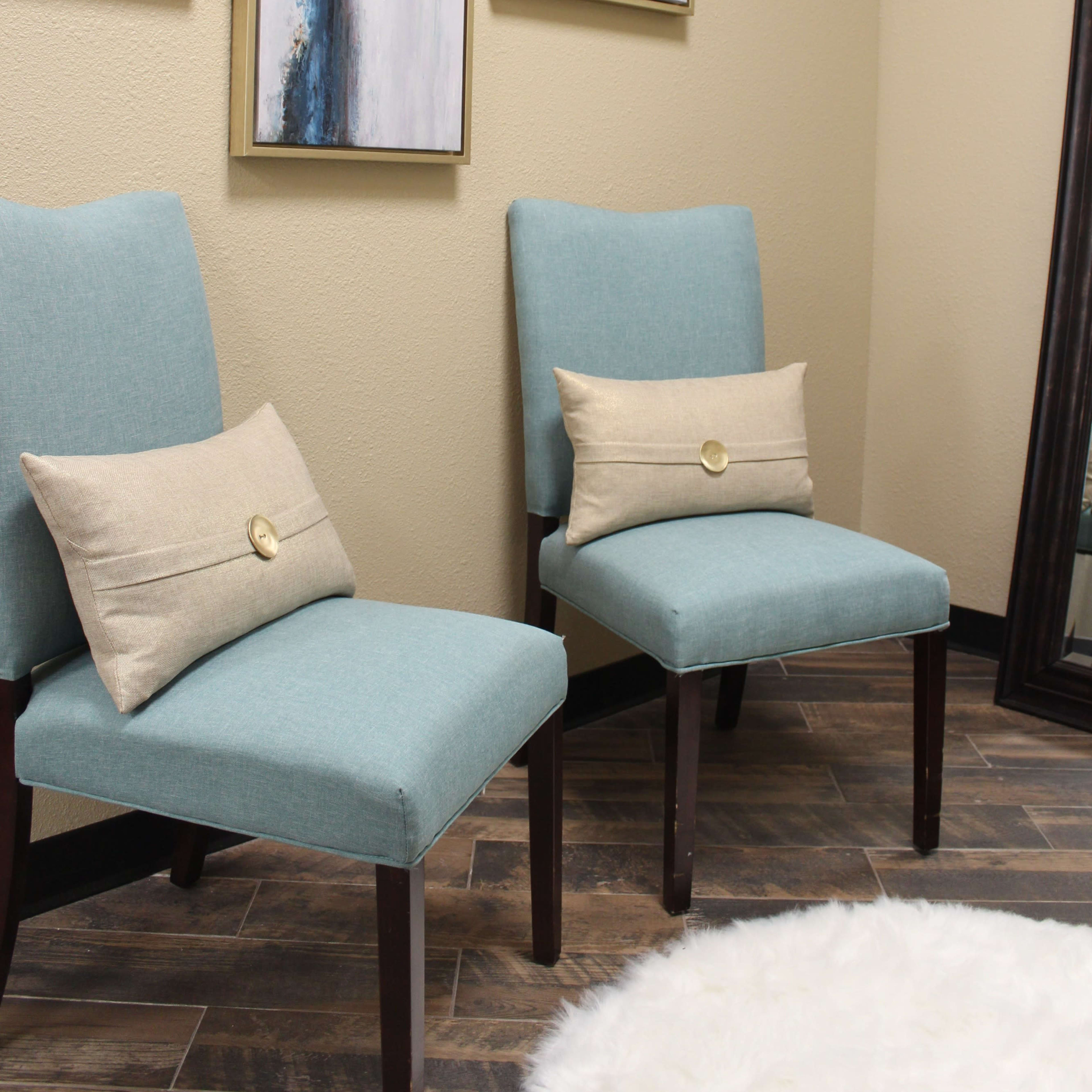 Two blue upholstered chairs with decorative pillows positioned against a wall decorated with framed abstract artwork.