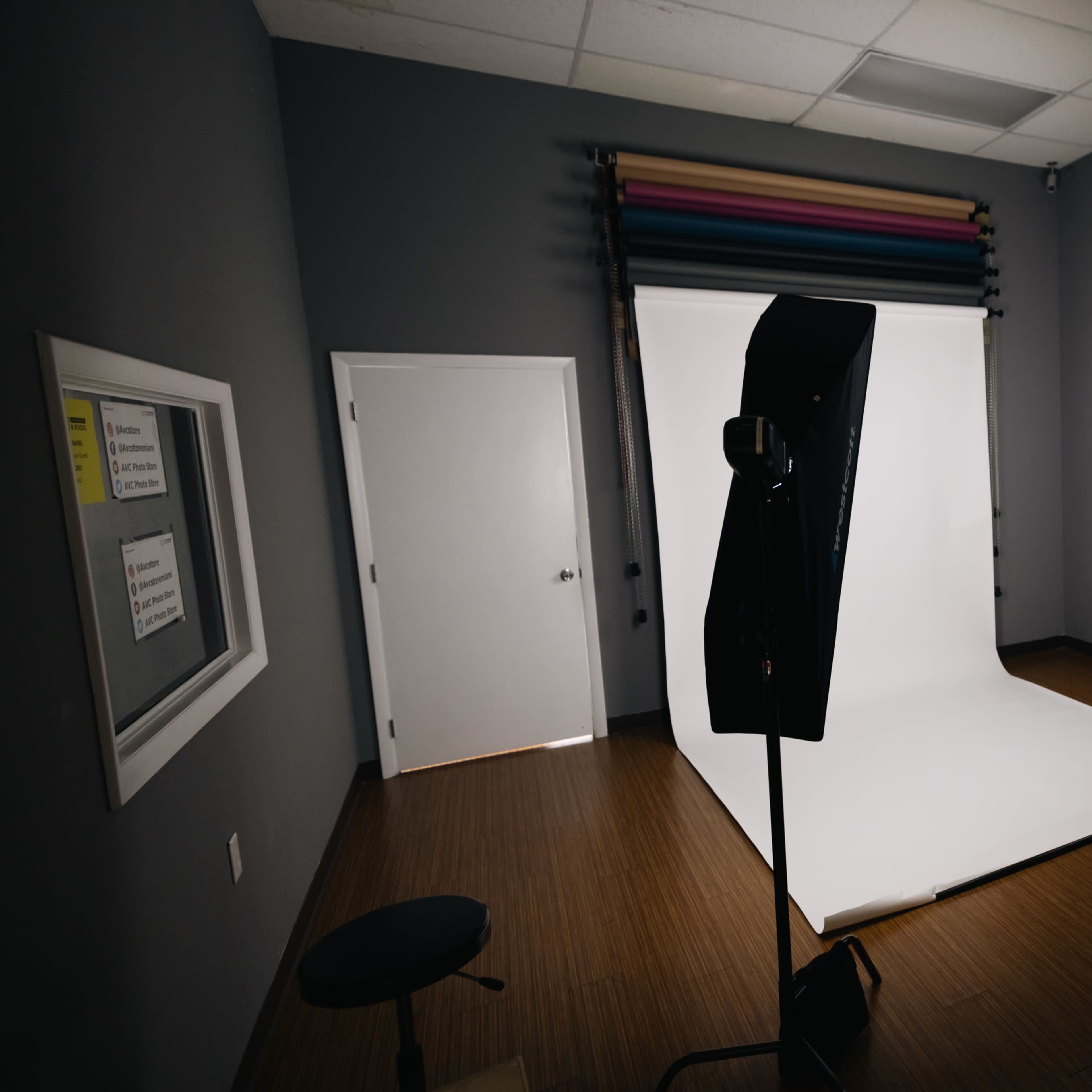 A photography studio with a white backdrop, two light sources, and a chair in the corner.