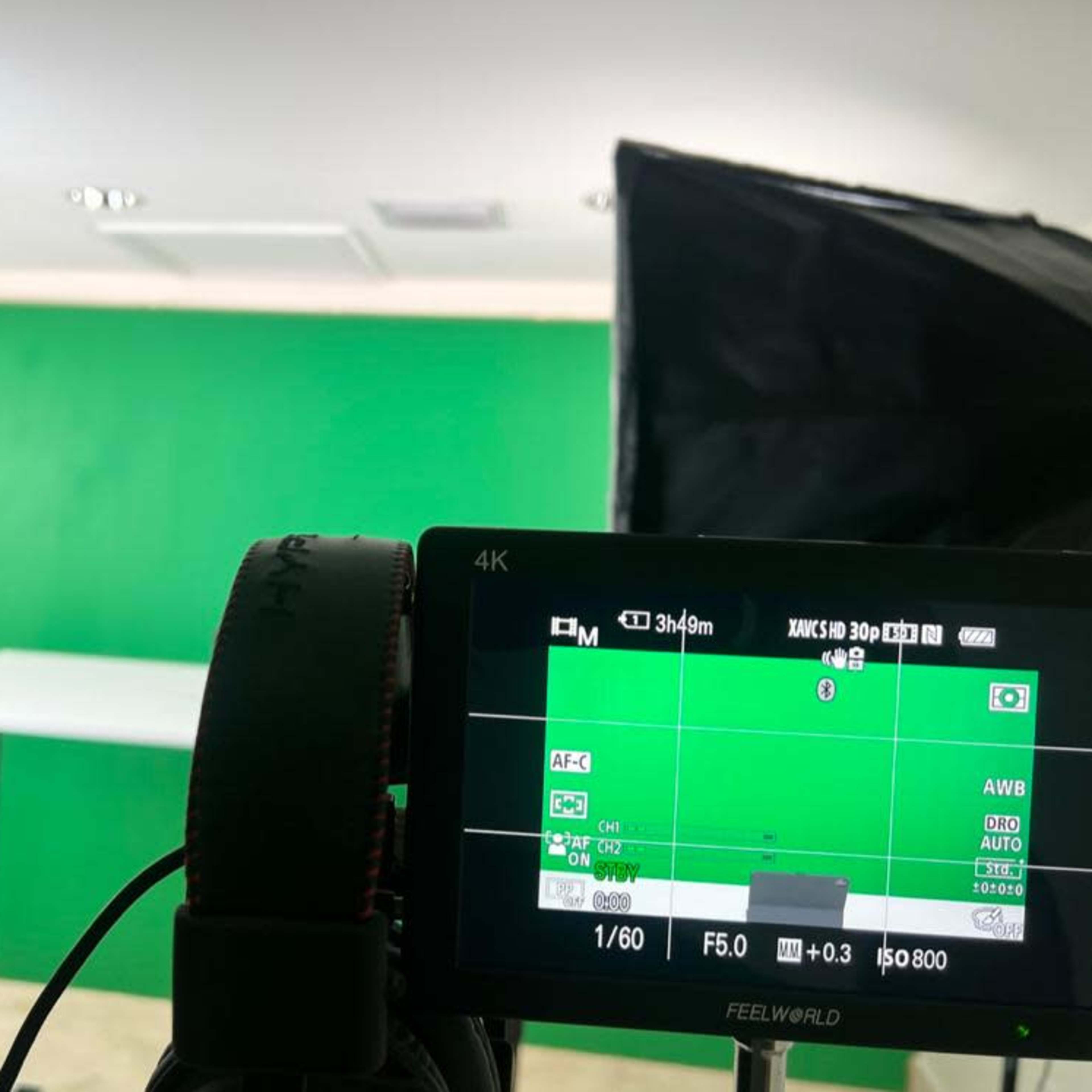 A camera setup with a monitor displaying a live view of a green screen and a table, with lighting equipment positioned on either side.