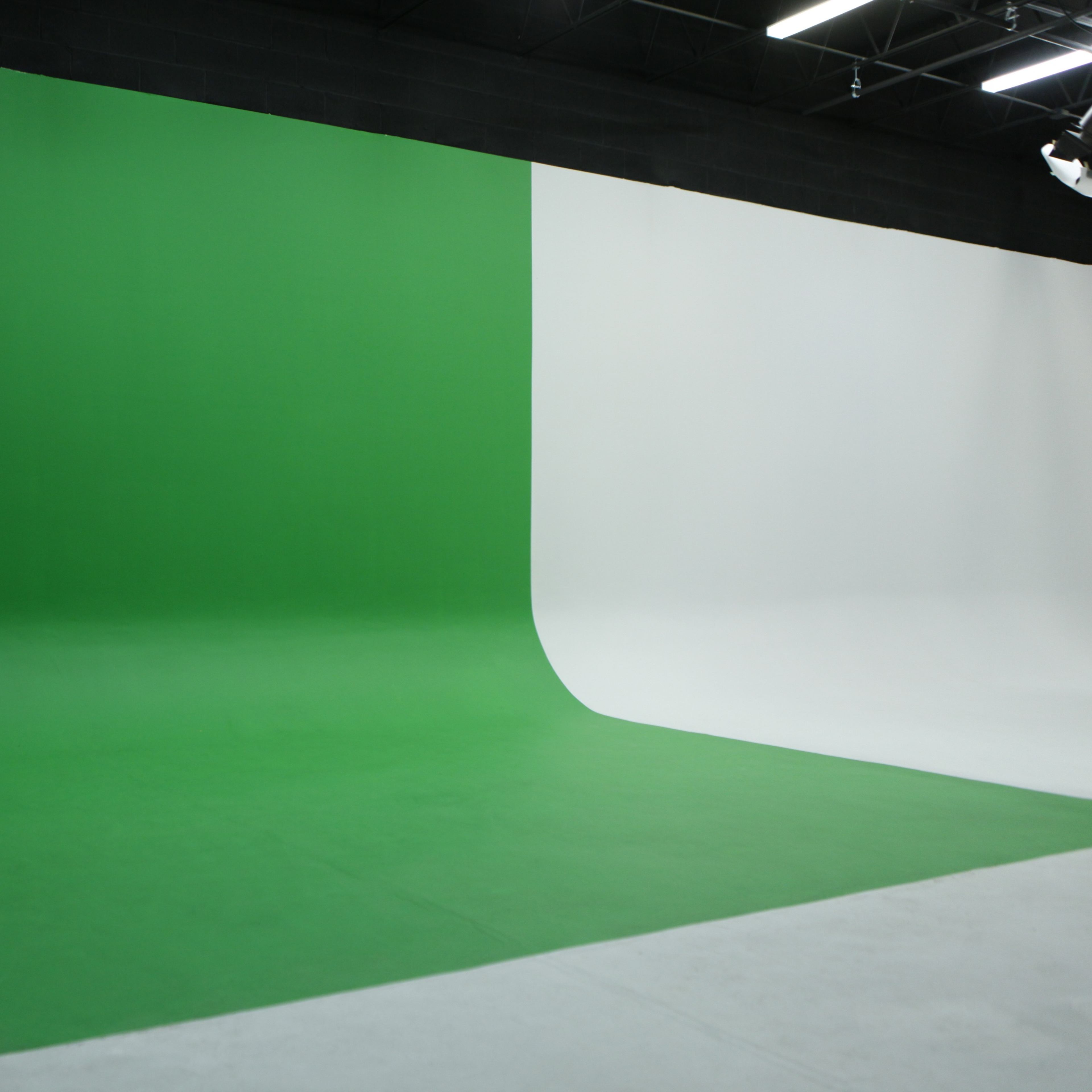 A studio features a green screen on one side and a white backdrop on the other.