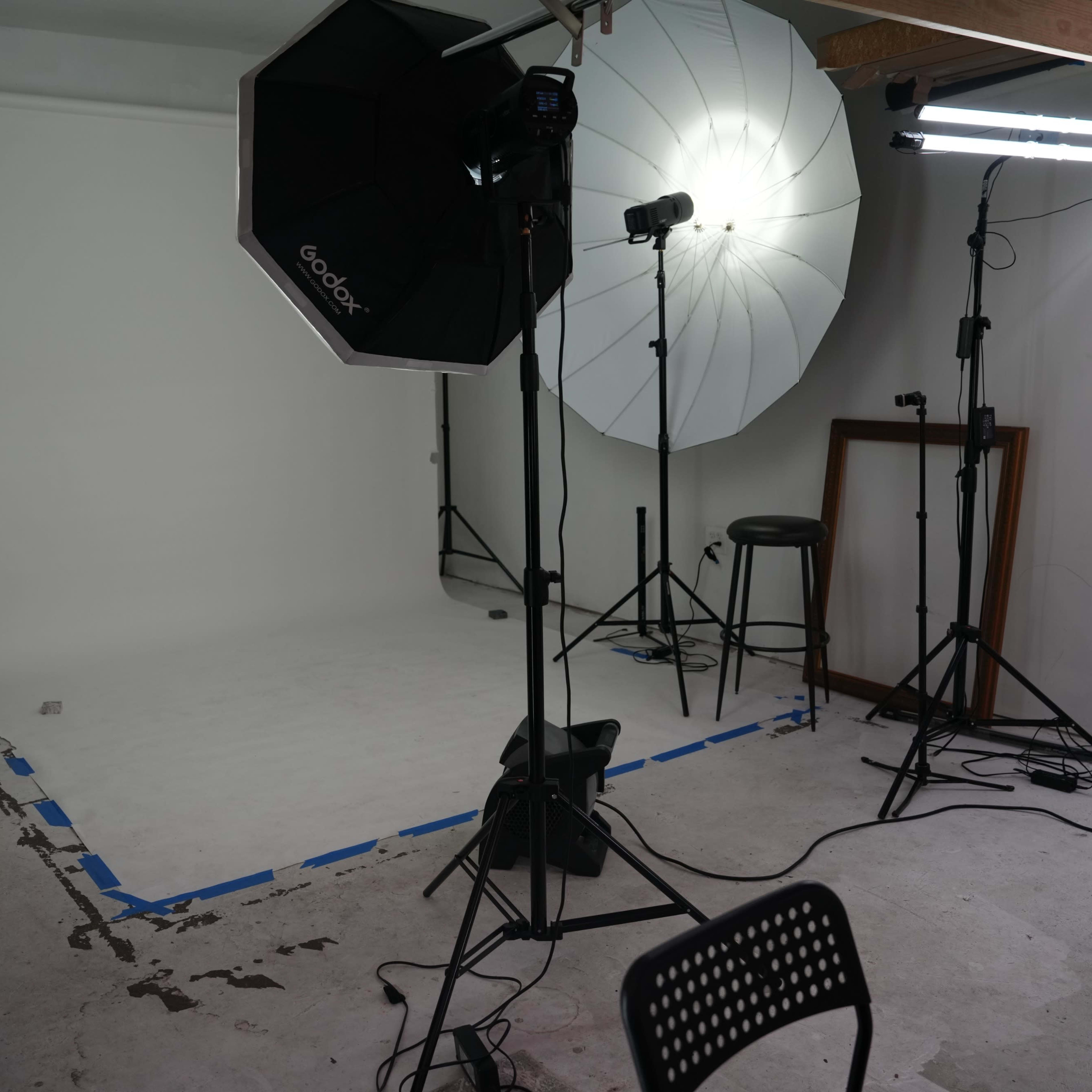 A photography studio setup with a blank white backdrop, lighting equipment, and a few stools and stands.