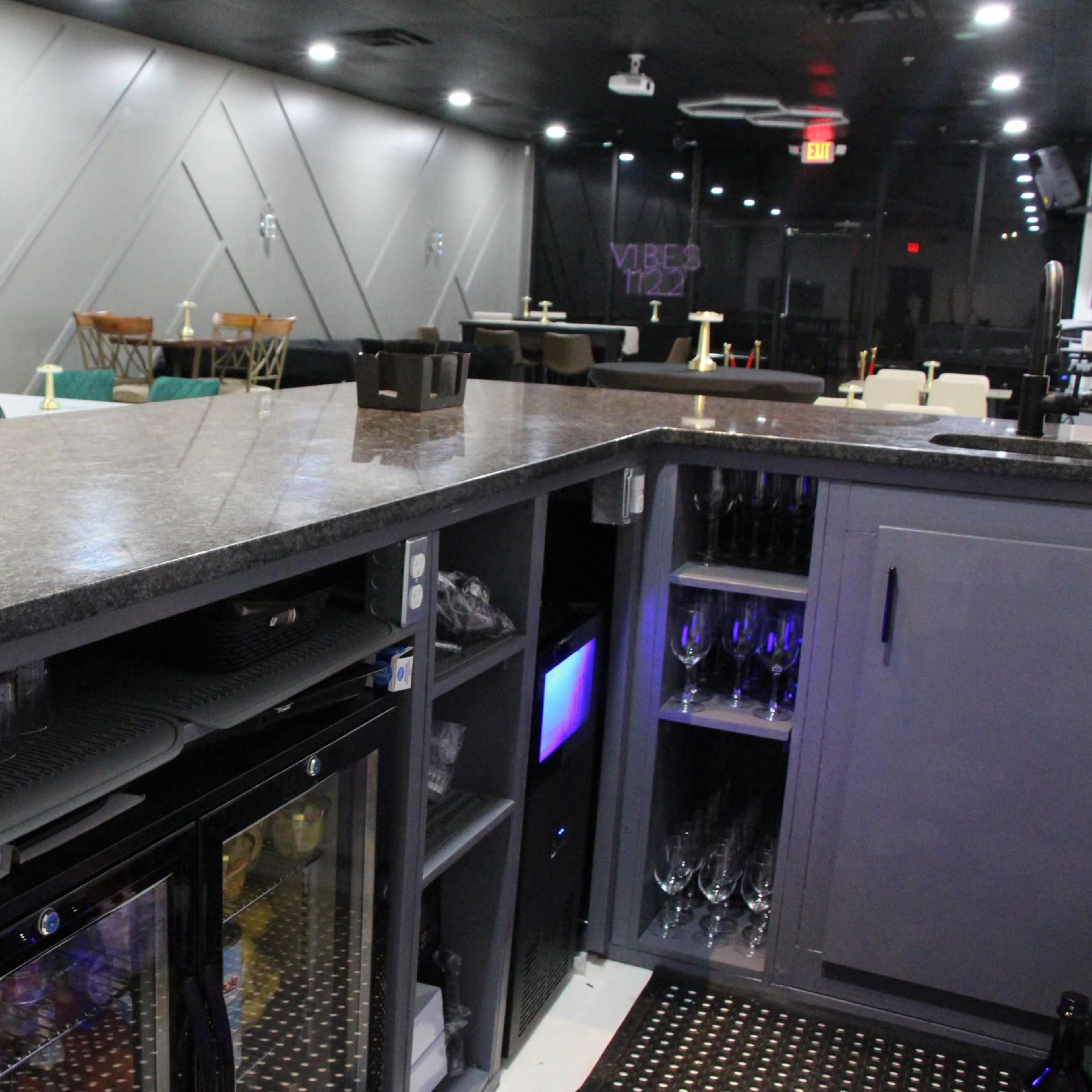 A modern bar area featuring a granite countertop, an under-counter fridge, and a display of glassware in a well-lit space with minimalist decor.