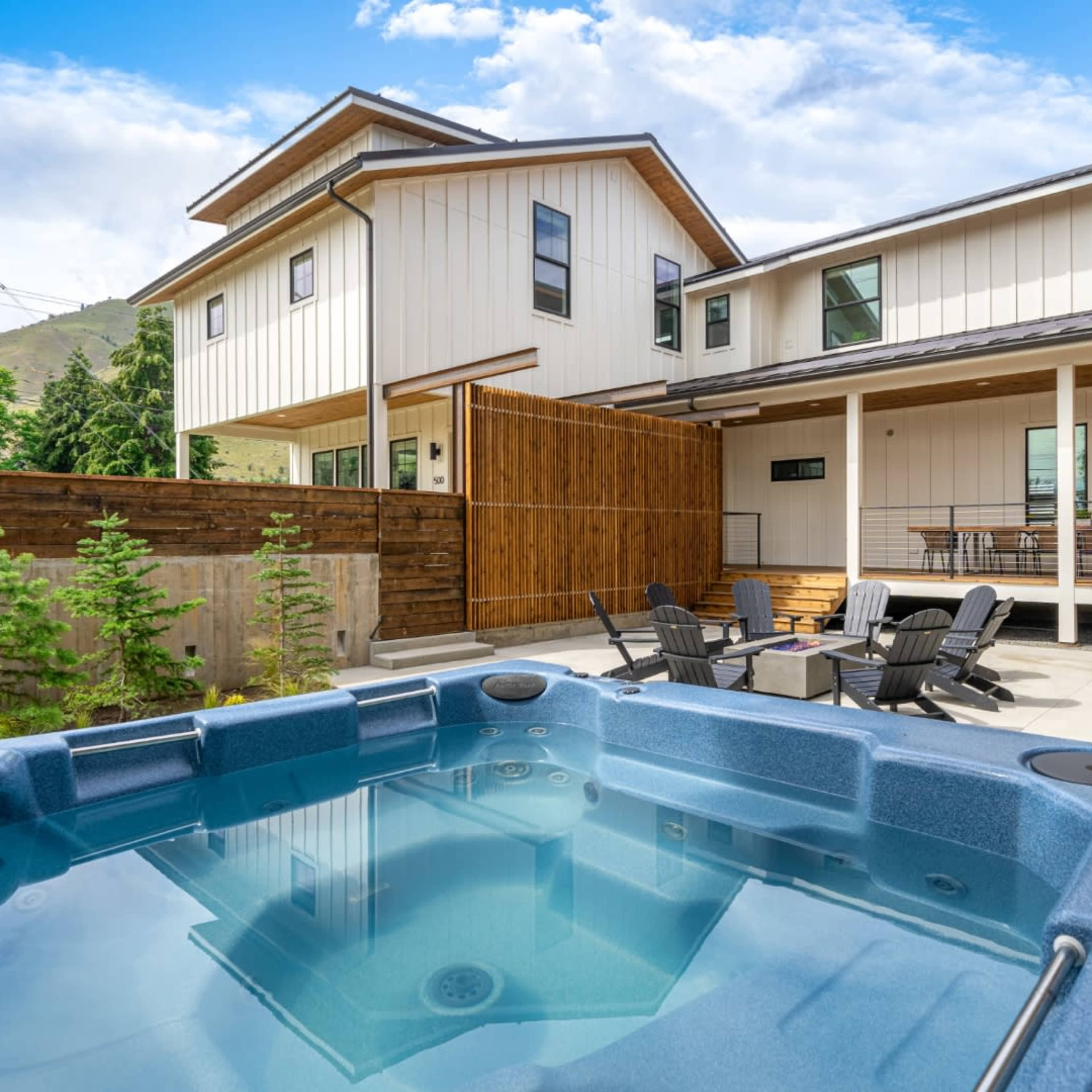 A hot tub is positioned in a private courtyard surrounded by modern buildings with outdoor seating and a grill area.