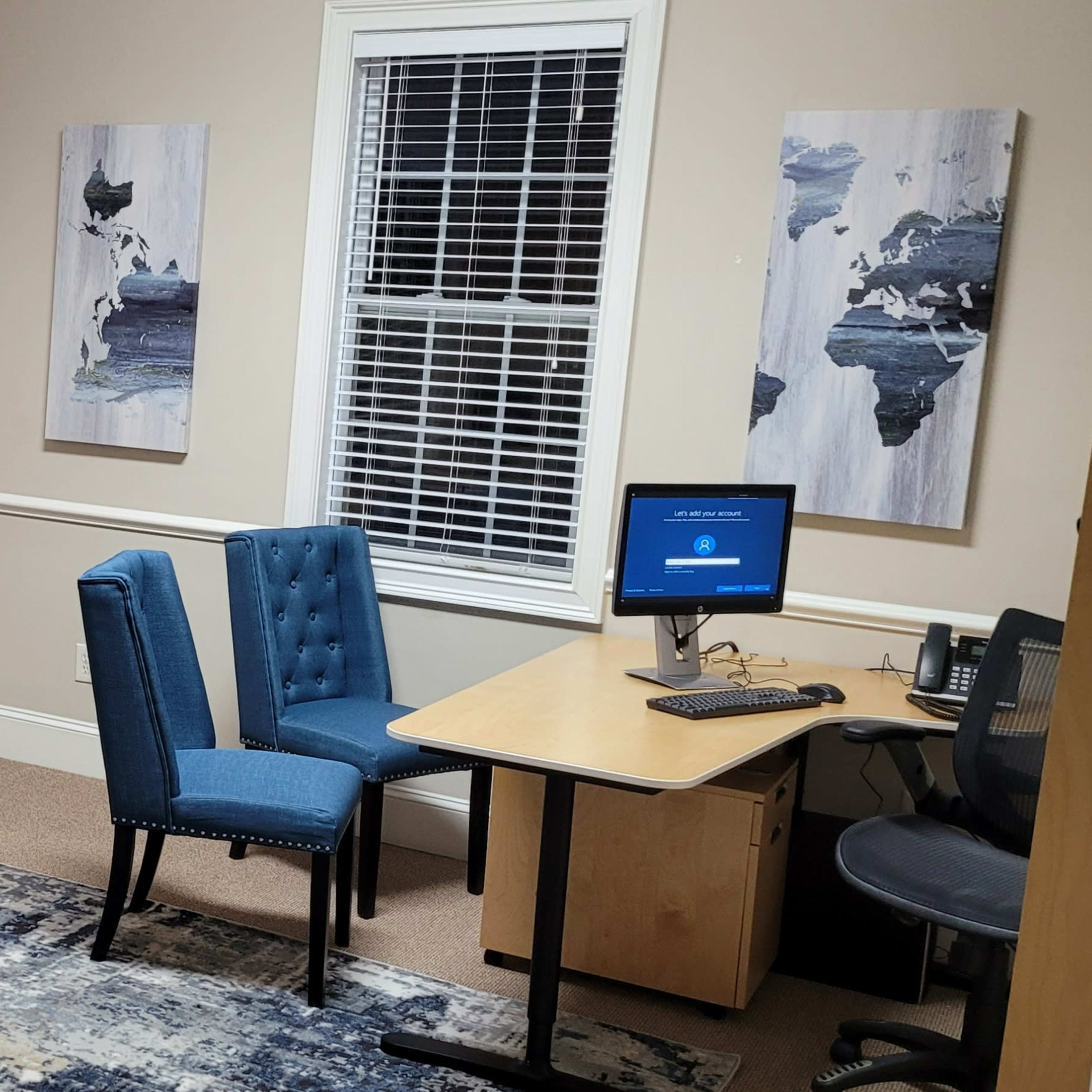 A small office space with blue chairs, a wooden desk and cabinets, and framed artwork on the walls.