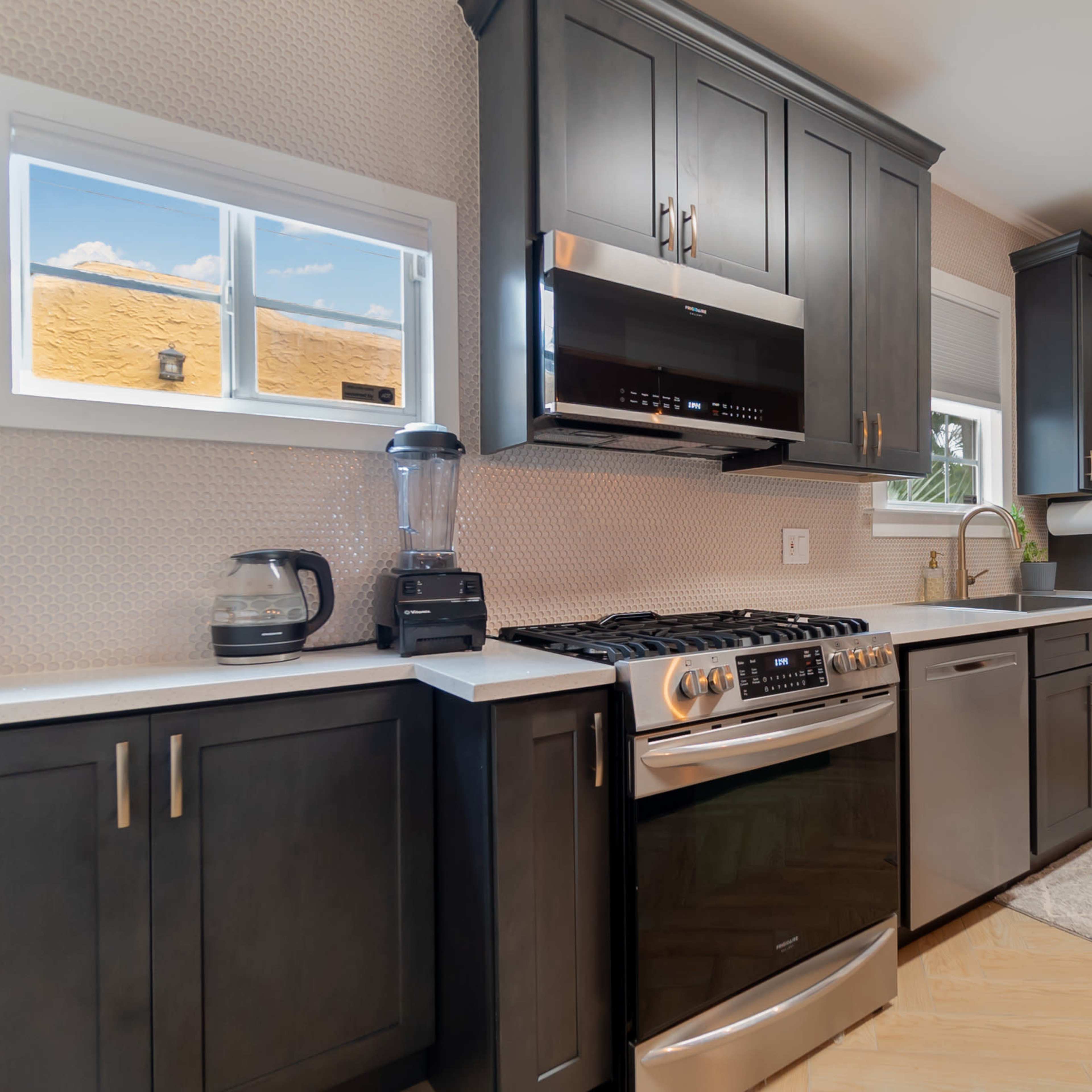 A modern kitchen featuring dark cabinetry, stainless steel appliances, and a light-colored countertop.