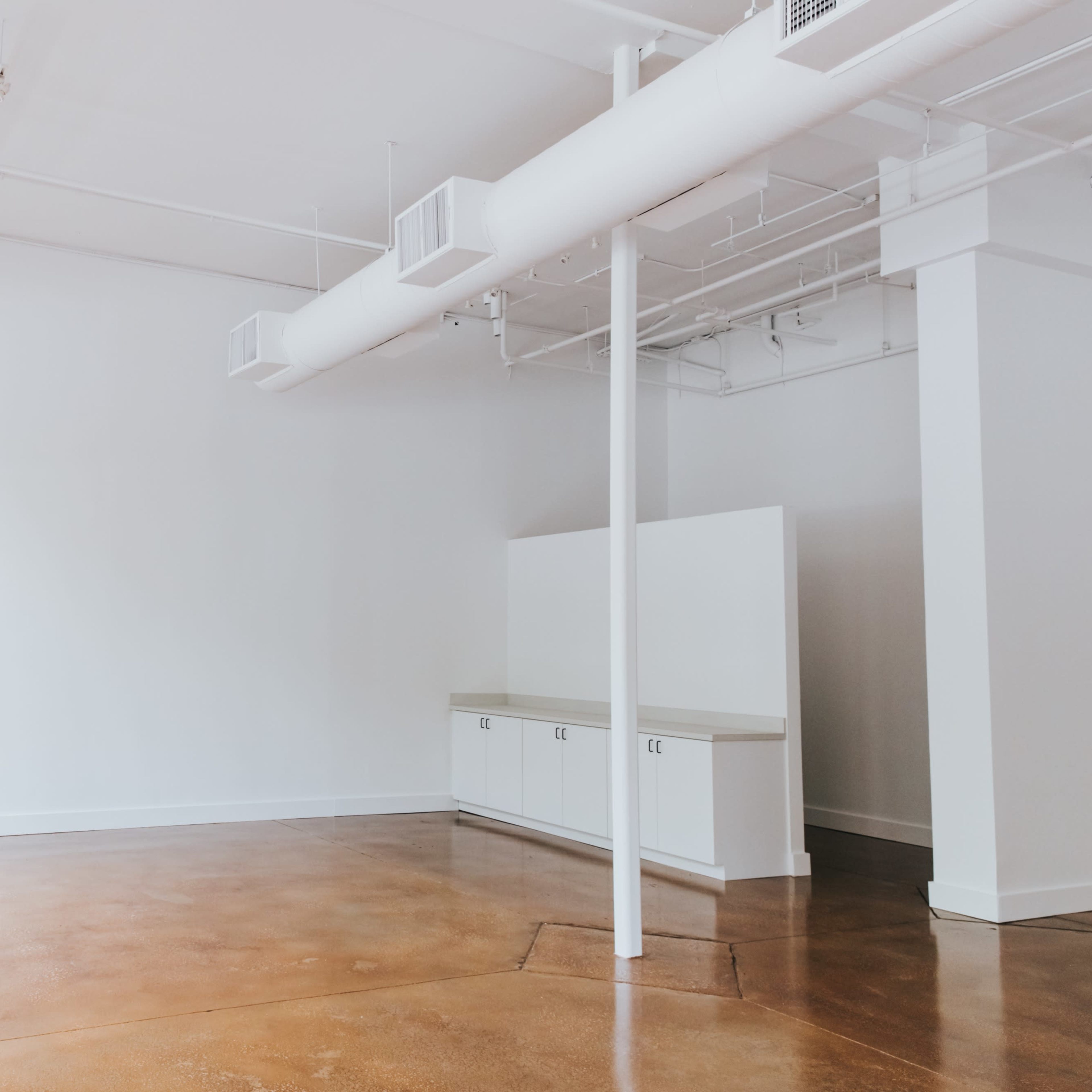 An empty, modern room with large windows, bare walls, and a small cabinet along one side.