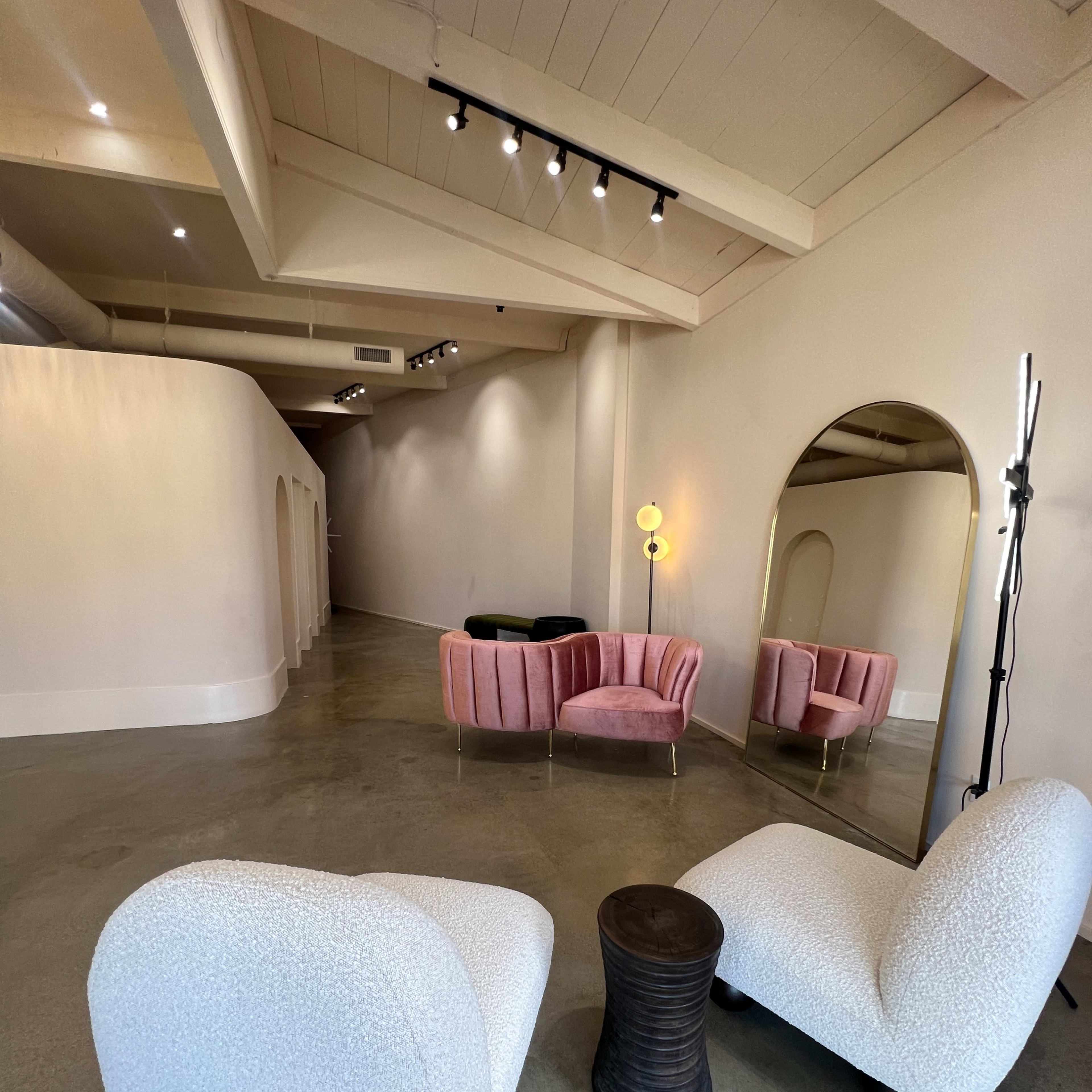 A modern interior space featuring two plush chairs, a small side table, and a curved hallway with a large mirror and soft lighting.