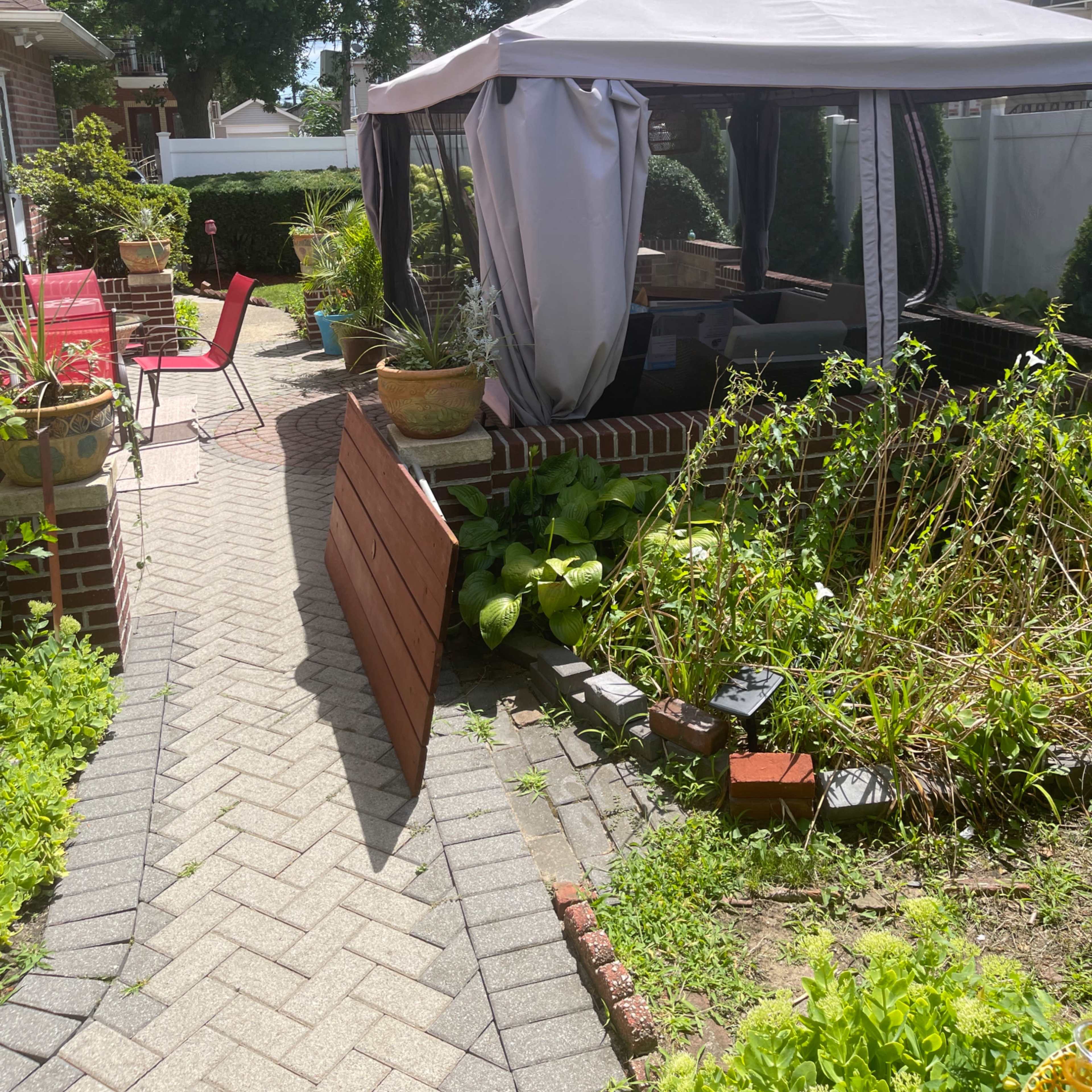 A pathway leads to a gazebo surrounded by potted plants and overgrown garden beds.