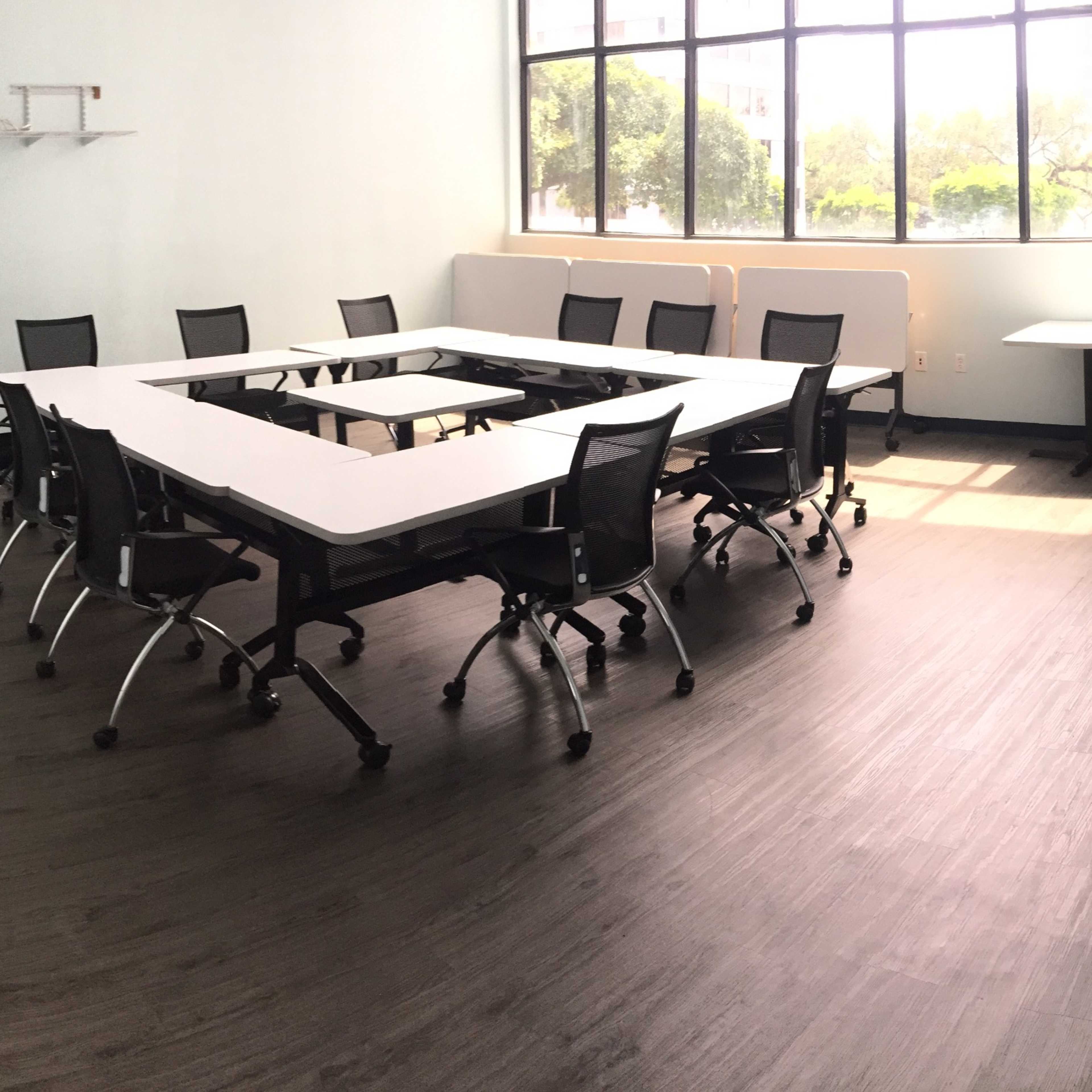 A meeting room with a rectangular table surrounded by black chairs, a whiteboard on the wall, and a banner in the corner.