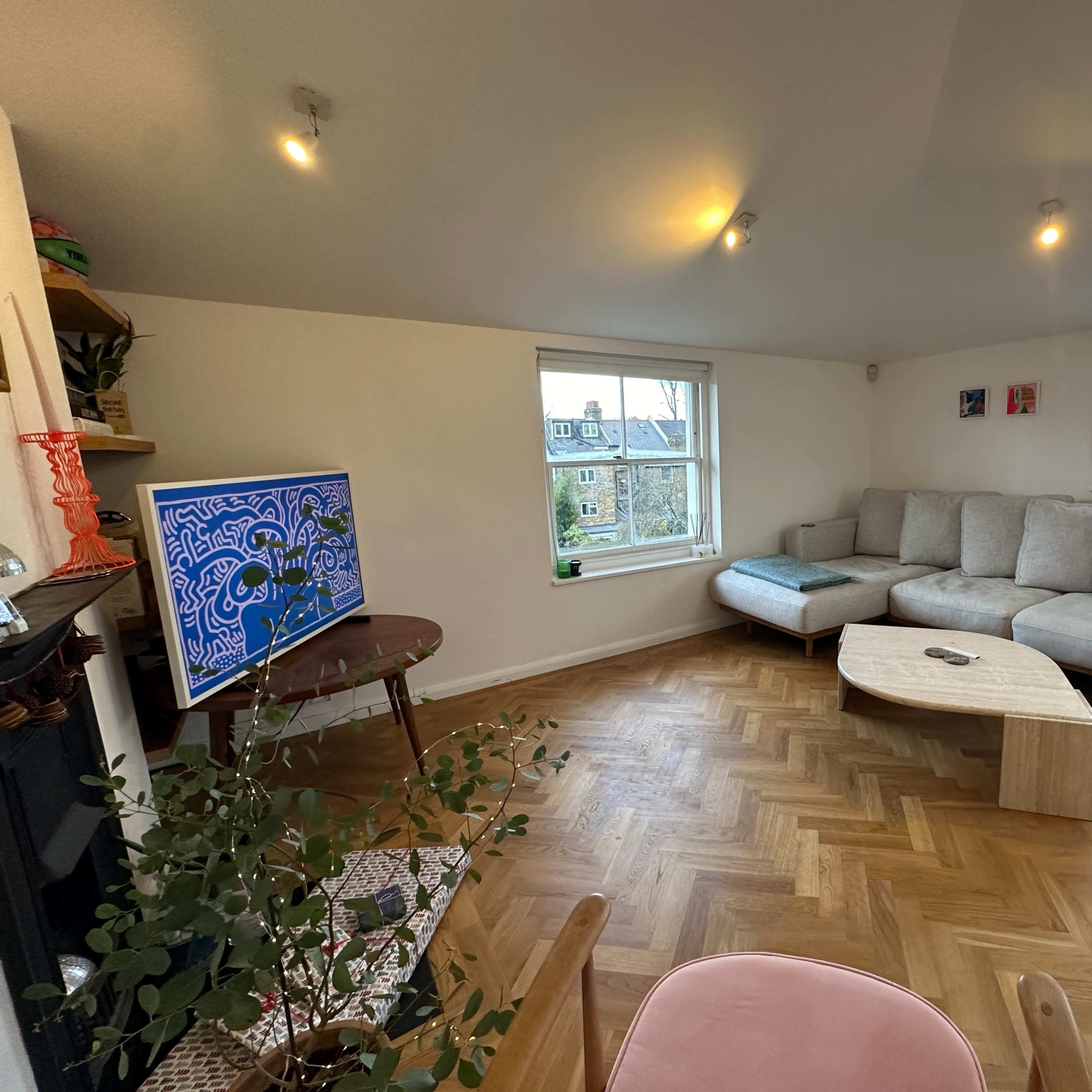 A cozy living room with a sectional sofa, a small coffee table, a television on a stand, and a large window letting in natural light.