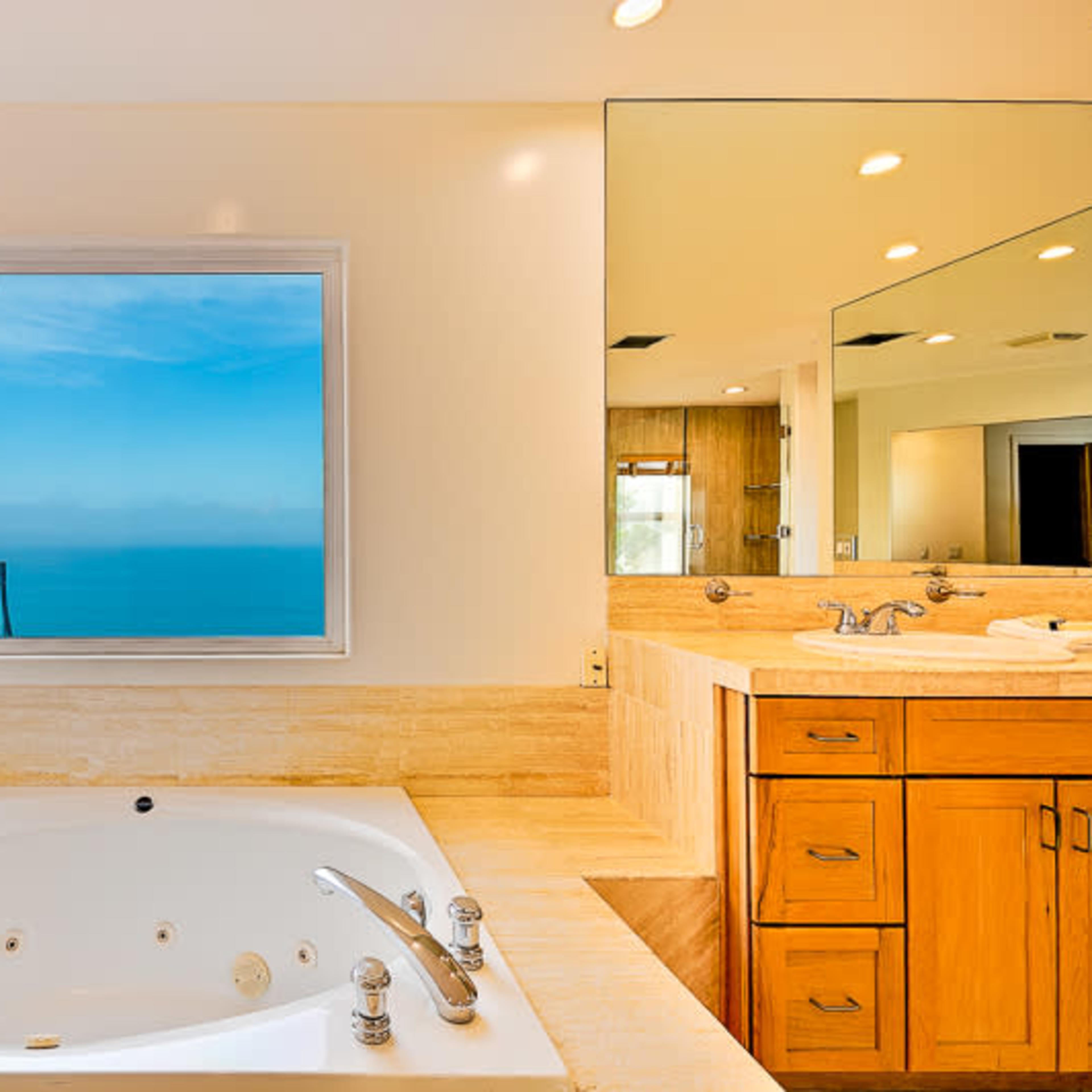 A bathroom featuring a large bathtub next to a window that offers a view of the ocean.
