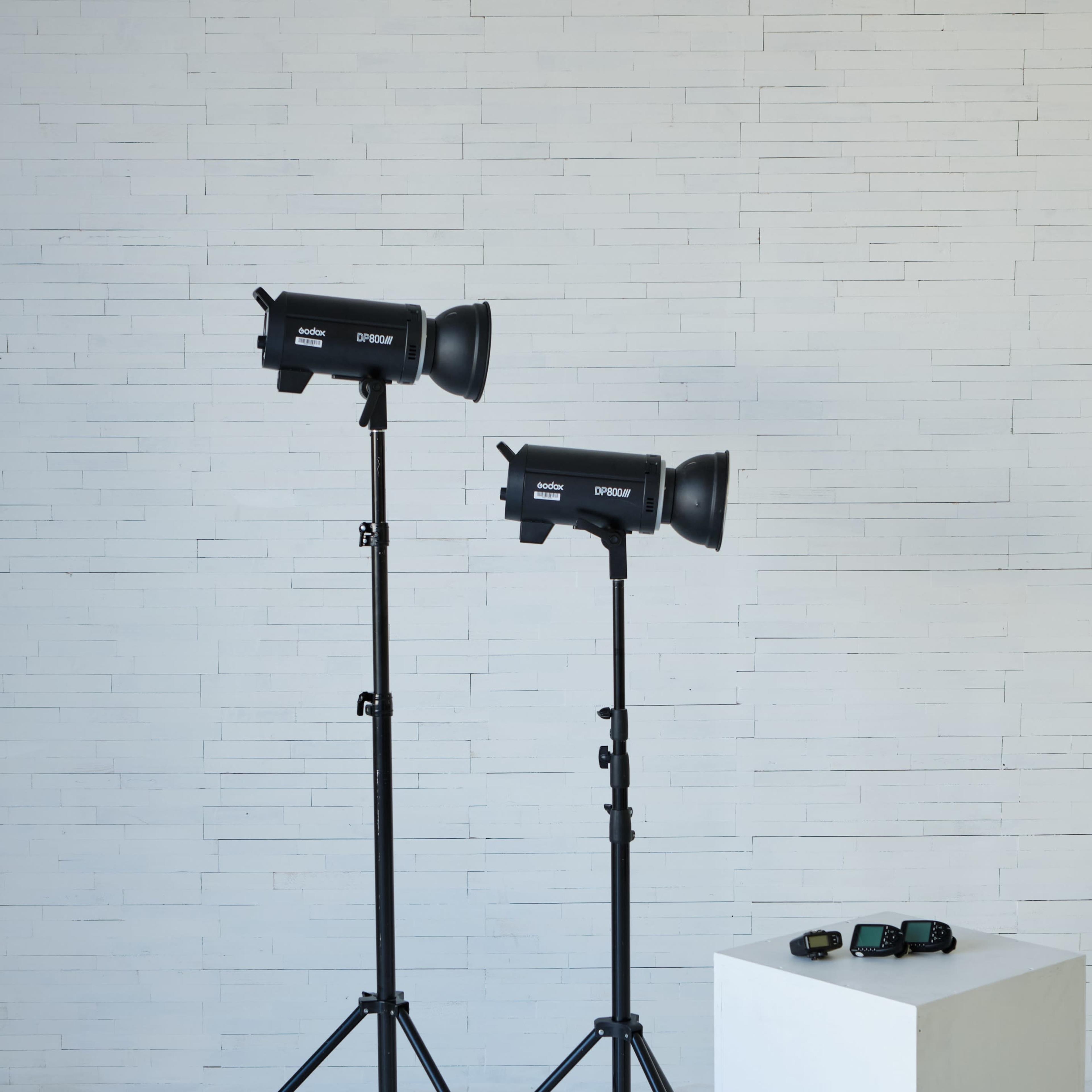 Two studio light stands are positioned beside a white pedestal in a minimalist setting.