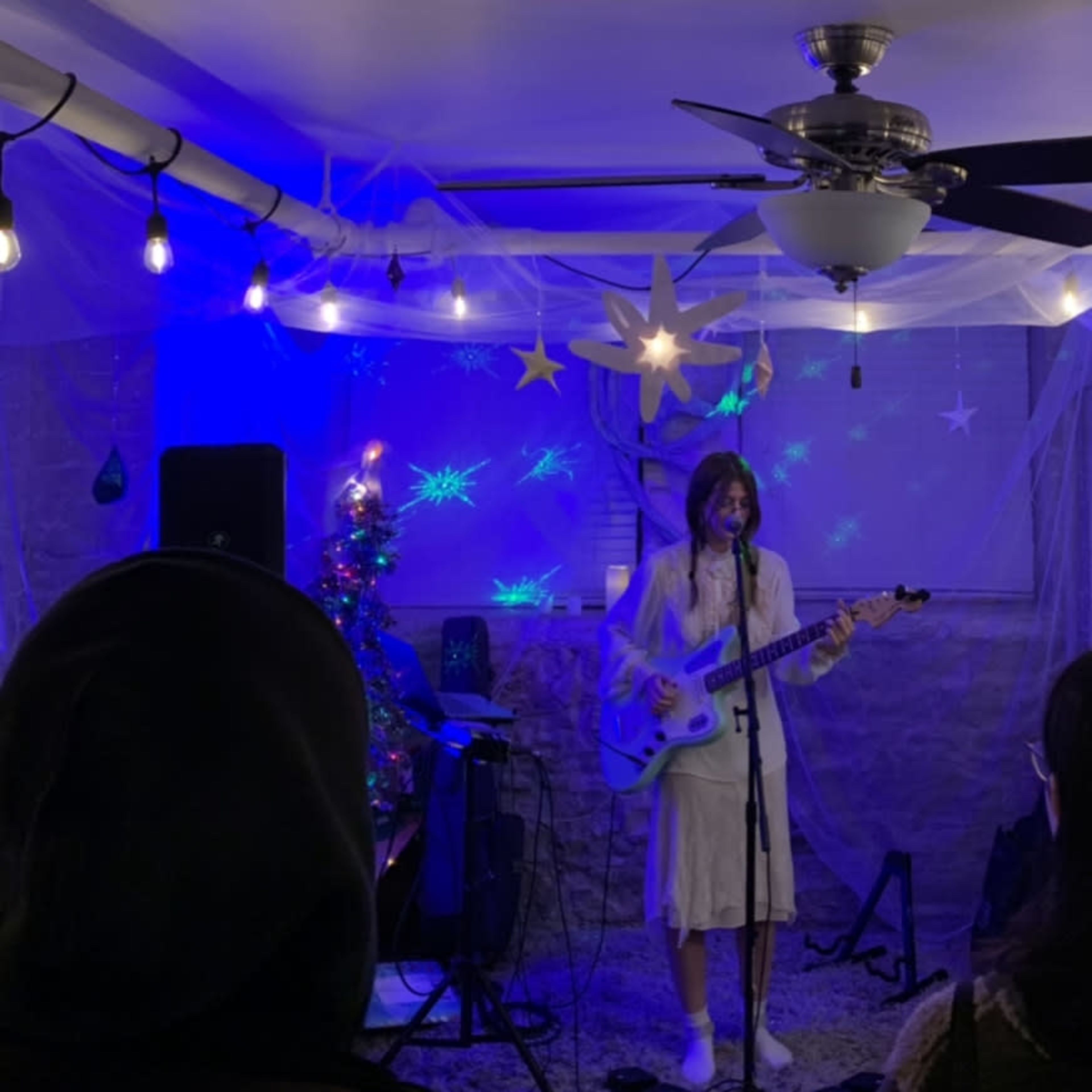 A musician performs on stage with a guitar in a dimly lit room decorated with festive lights and a small Christmas tree.