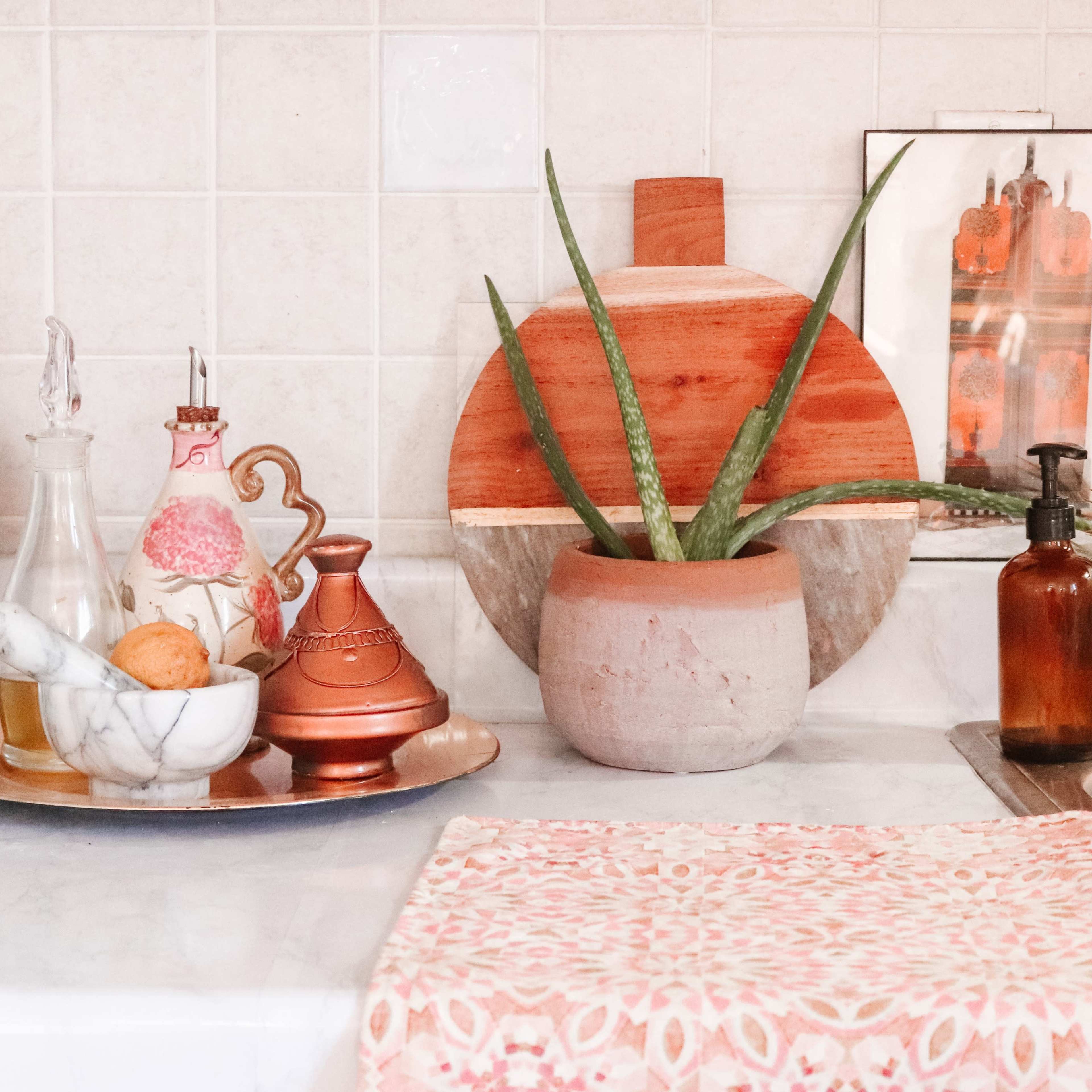 A kitchen counter adorned with decorative items, including plants, glass containers, a marble mortar and pestle, and copper accents.