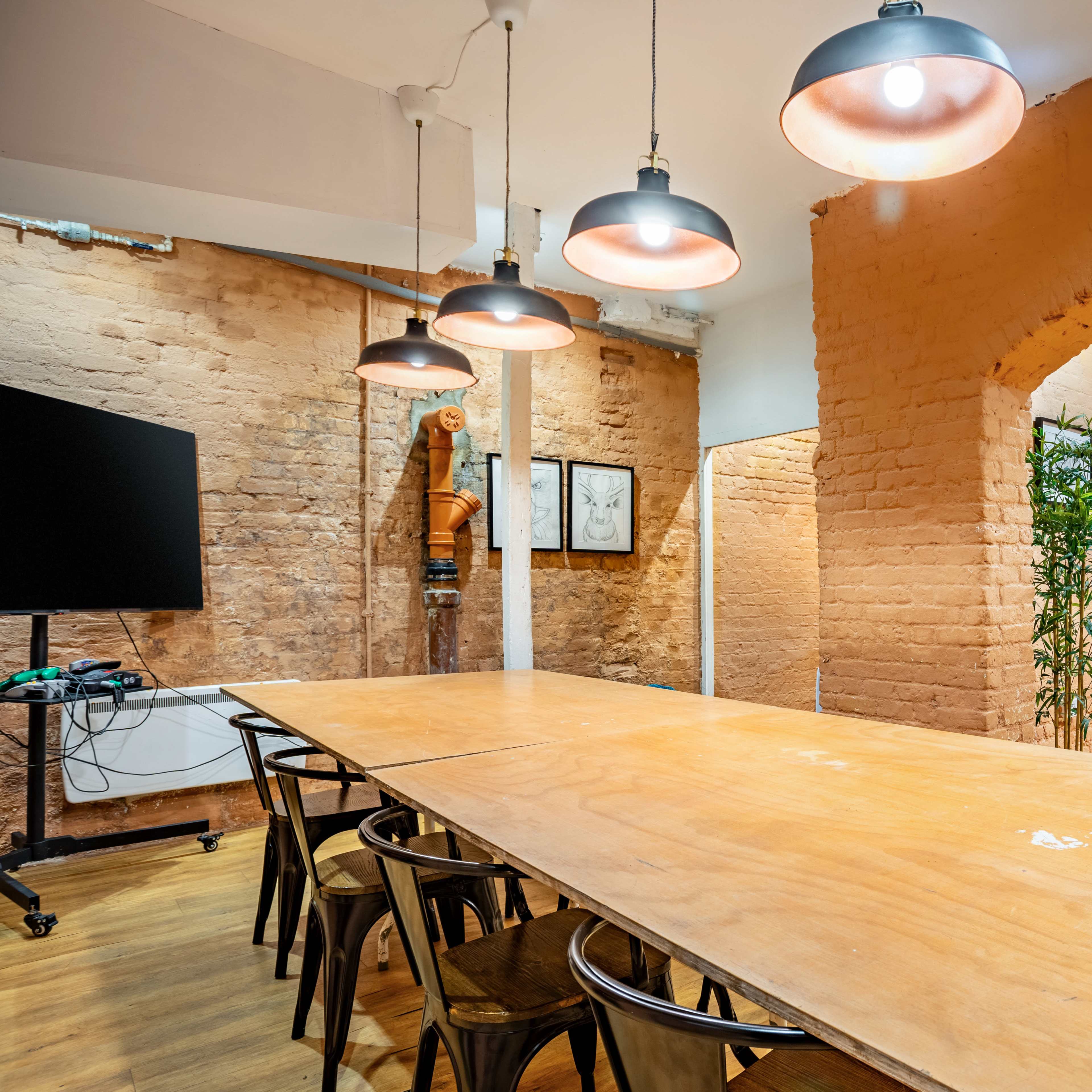 A spacious, well-lit meeting room with a long wooden table, surrounded by chairs, and features warm orange brick walls illuminated by several pendant lights.
