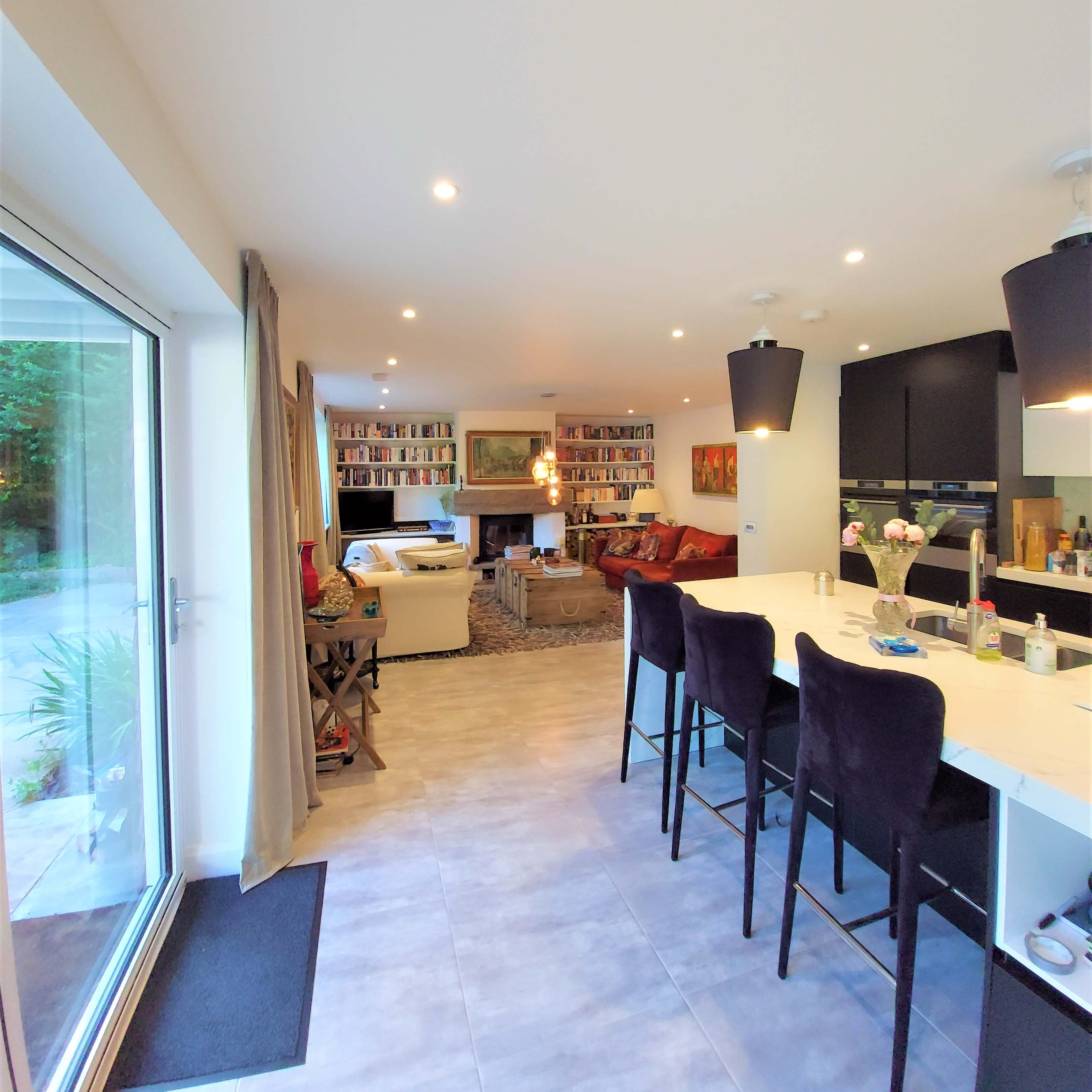 A modern open-concept living area with a kitchen bar, seating area, and bookshelves in the background.