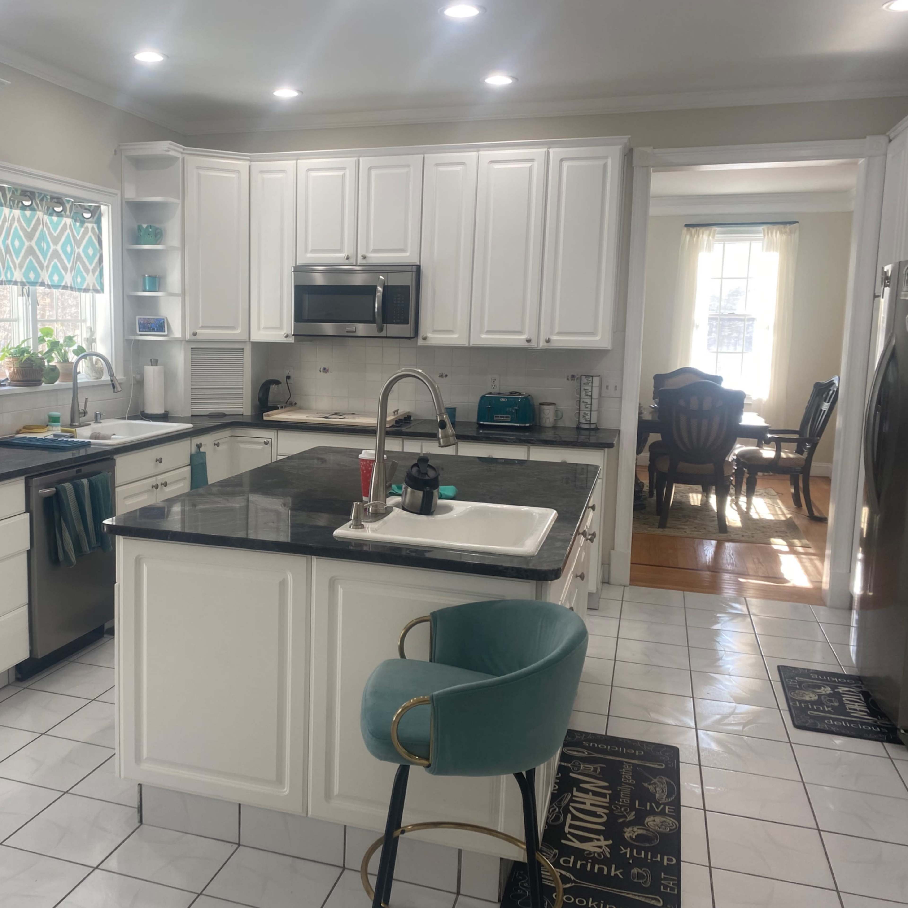 A modern kitchen with white cabinetry, a black countertop, and a dining area visible through an open layout.