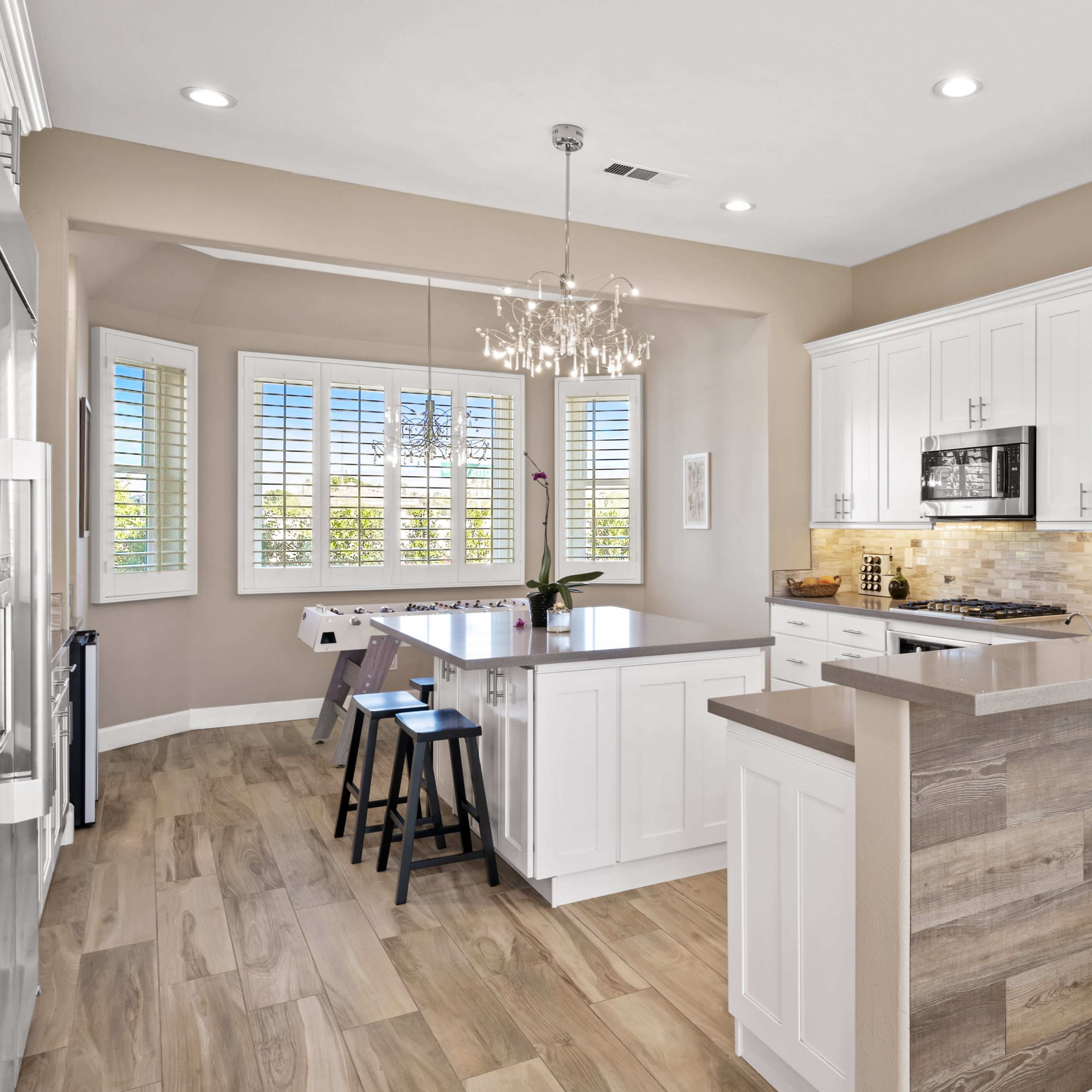 A modern kitchen with white cabinets, a central island, and large windows overlooking a patio area.