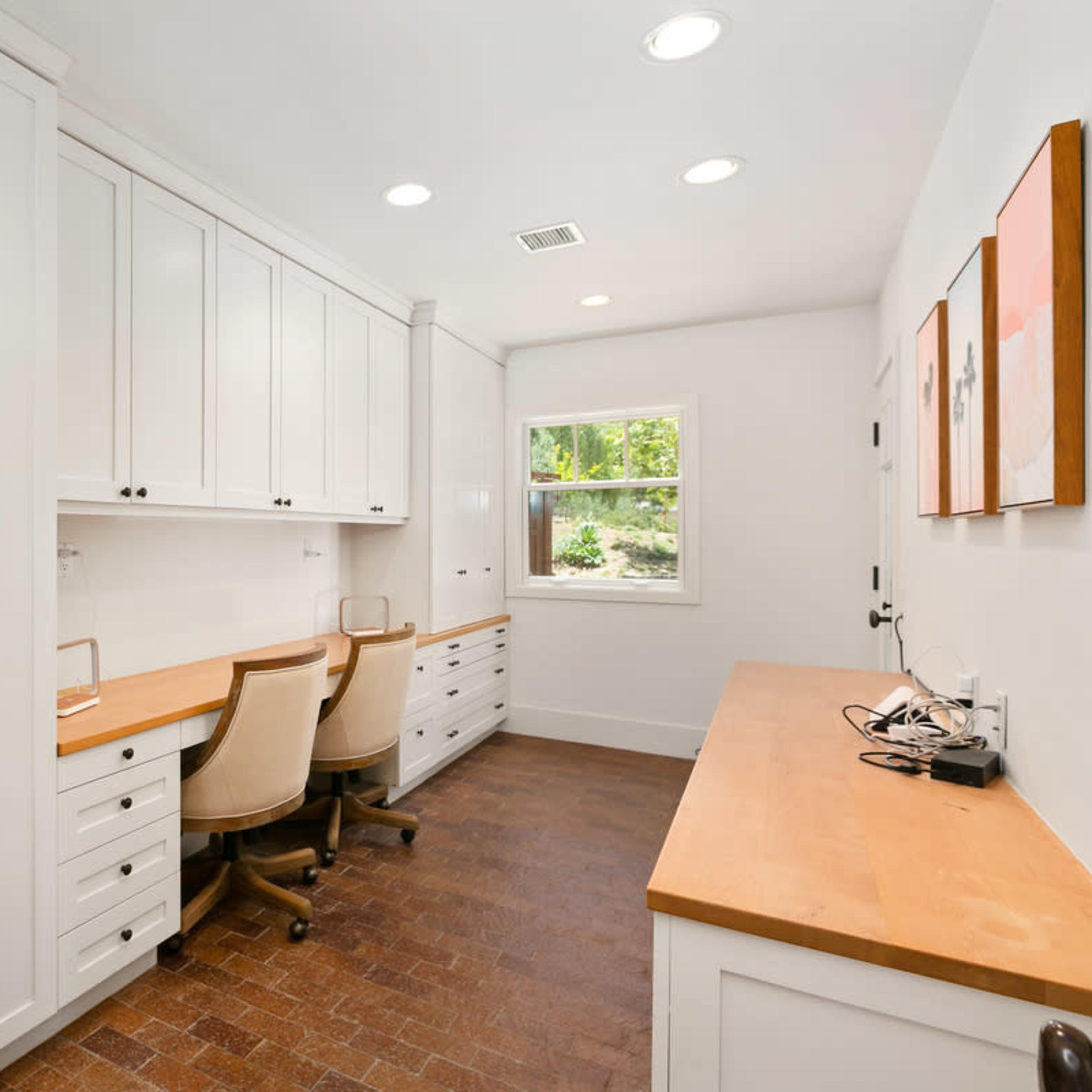 A bright home office with two workstations and built-in cabinetry along the walls.