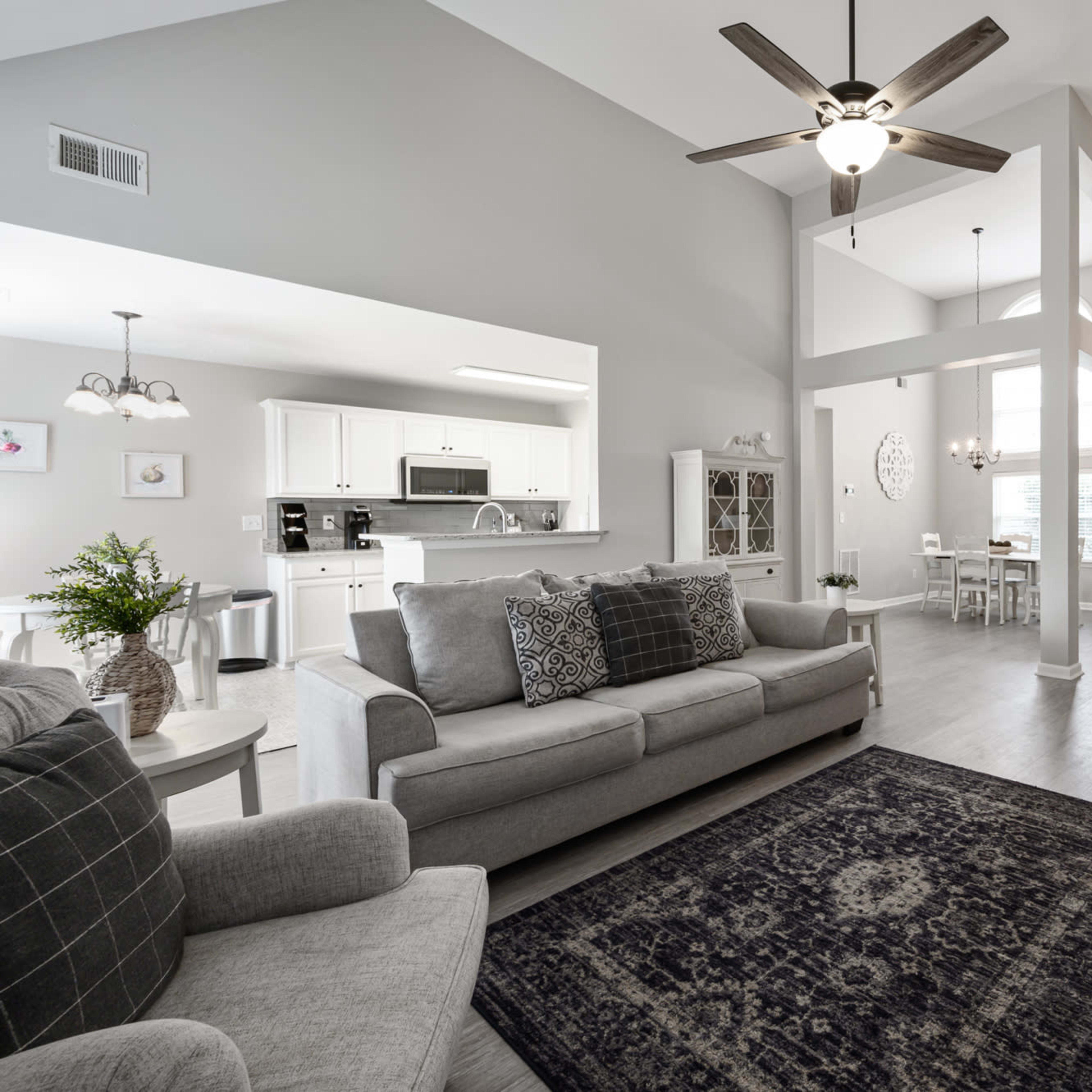 A bright, open living area featuring a light-colored sofa, a patterned area rug, and a dining space with a table in the background.