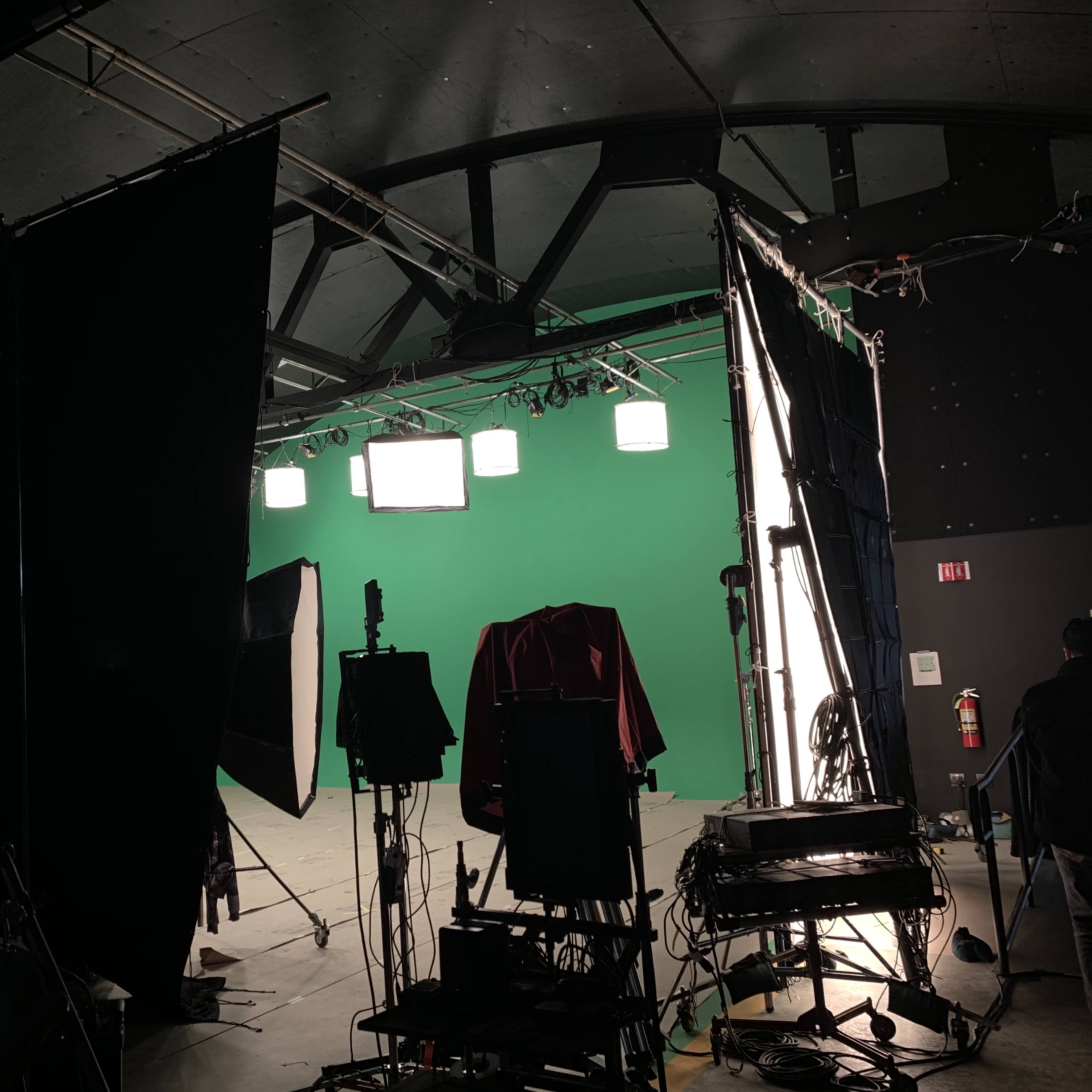 A film studio setup with a green screen, lighting equipment, and various props on the floor.
