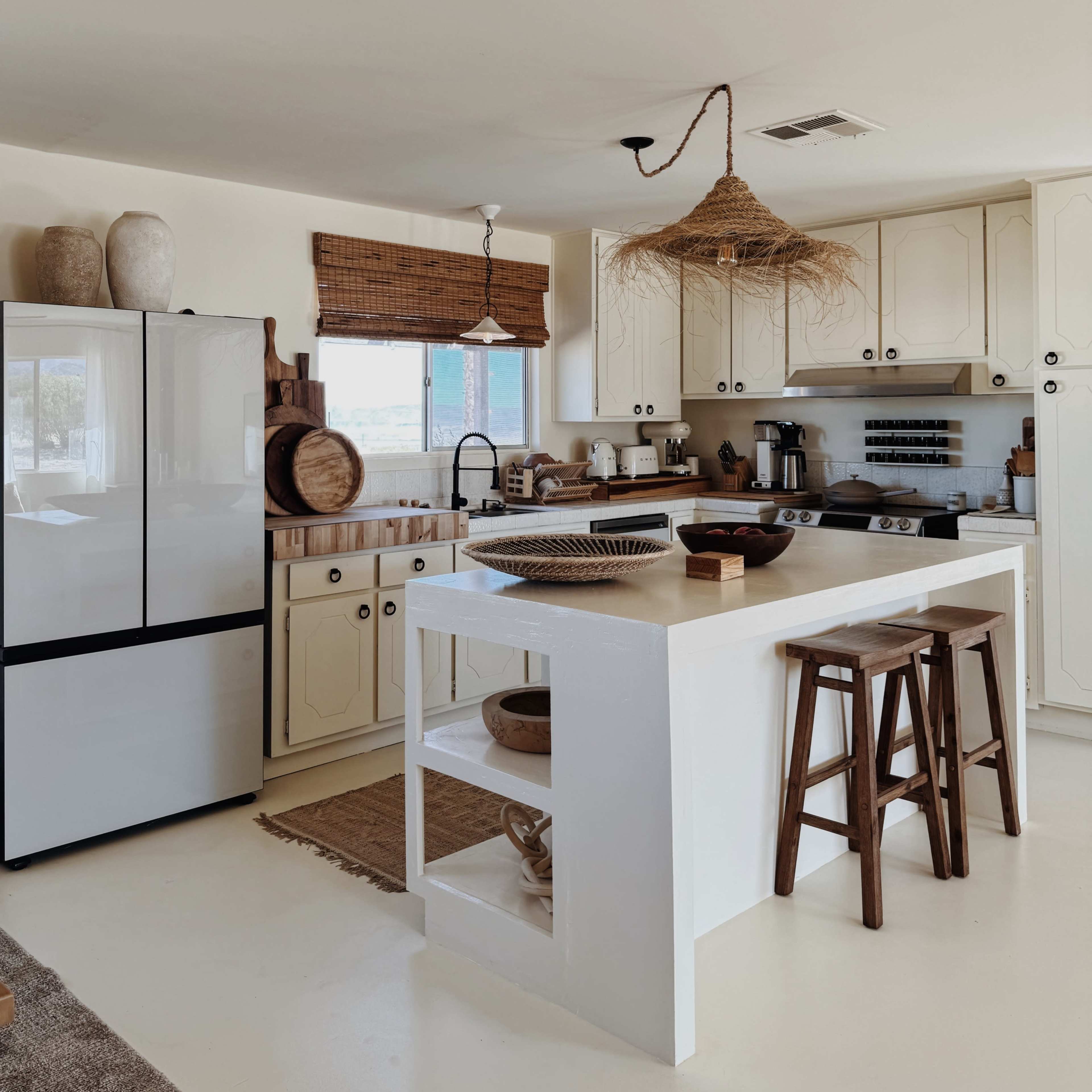 A bright kitchen featuring a white countertop island with wooden stools, a refrigerator, and rustic decor elements.