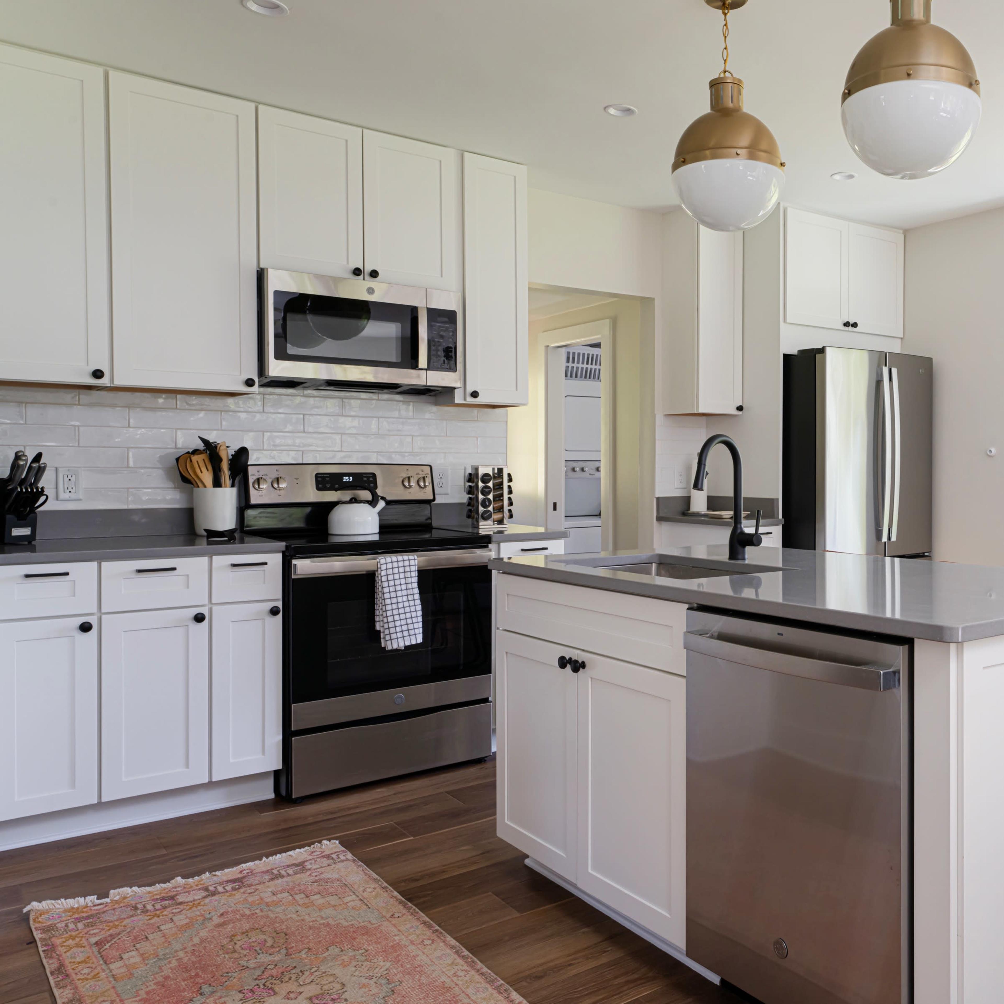A modern kitchen with white cabinetry, stainless steel appliances, a central island with a gray countertop, and a window overlooking a green outdoor landscape.