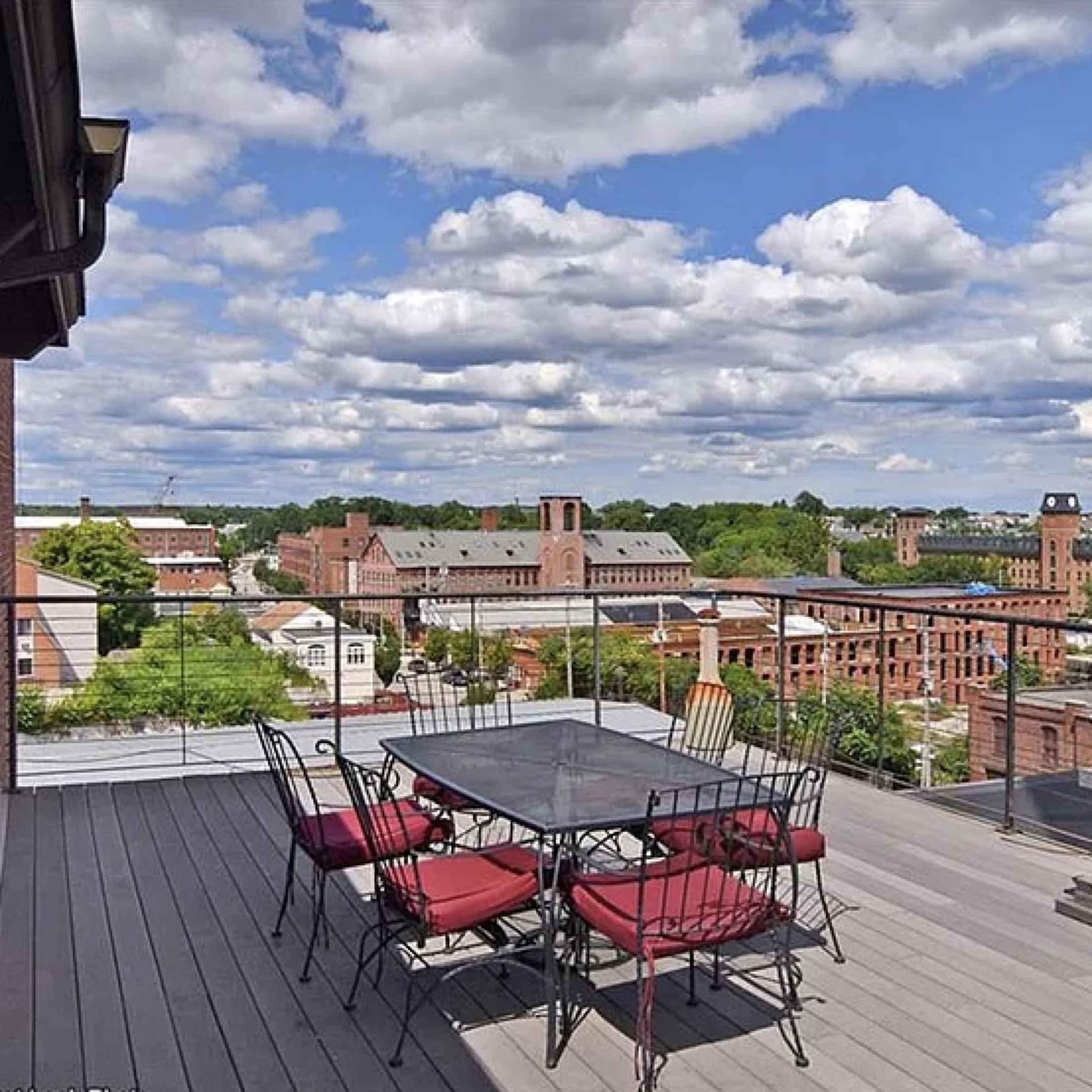 A rooftop patio with a metal dining table and chairs overlooking a cityscape under a cloudy sky.