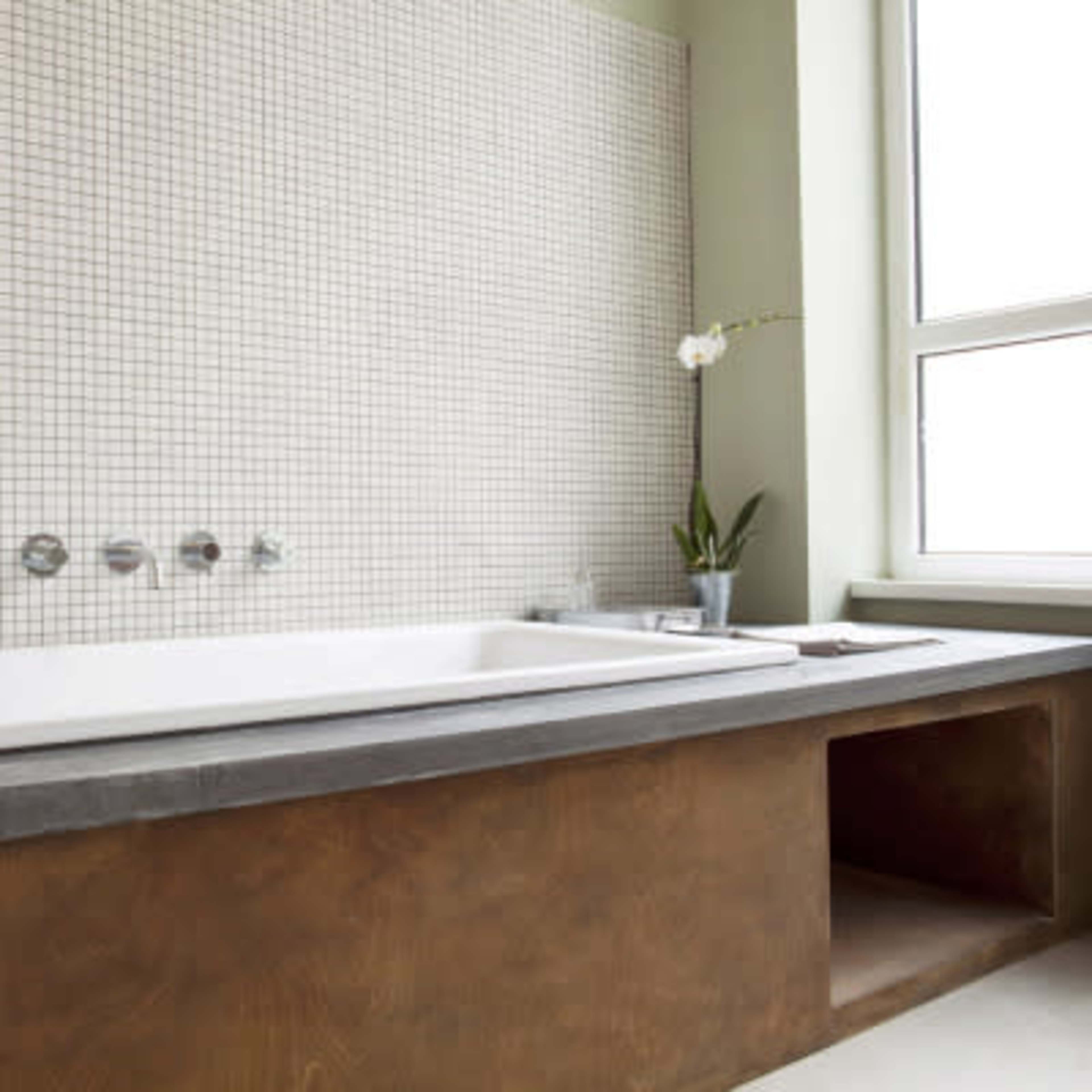 A modern bathroom features a large, rectangular bathtub with a tiled wall and a window that lets in natural light.