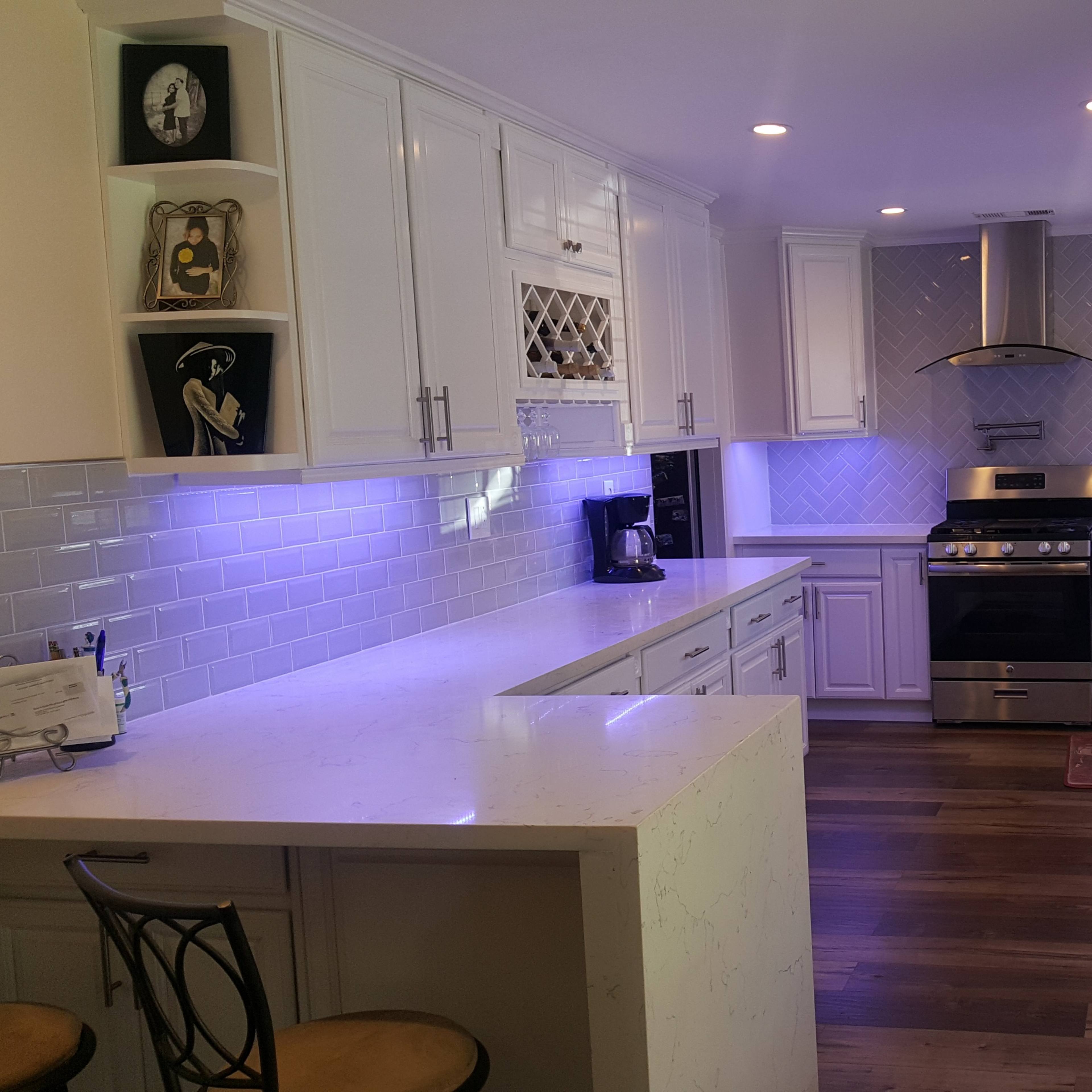 A modern, white kitchen featuring stainless steel appliances, a large island with stools, and bright lighting.