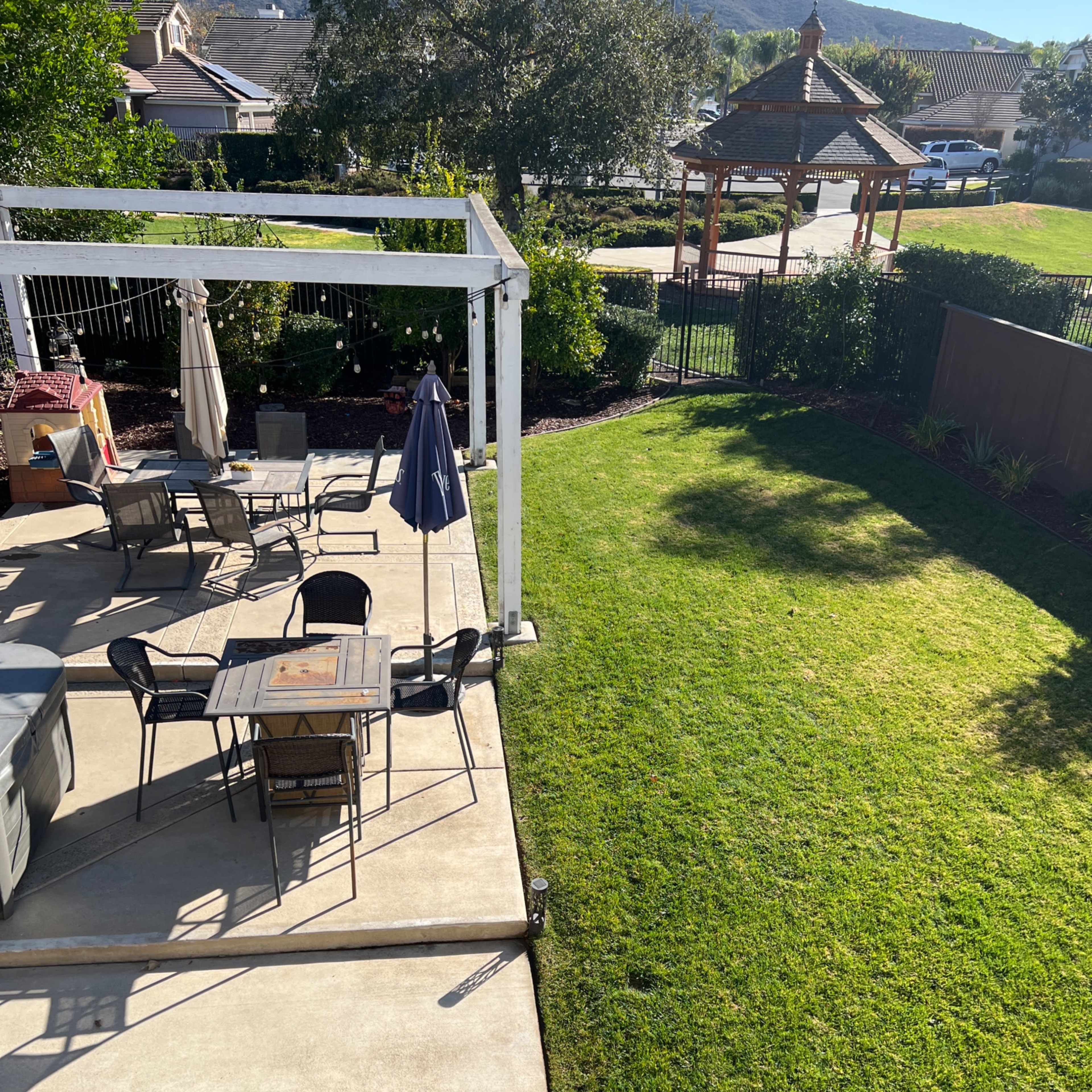 A backyard patio with a table and chairs, a patio umbrella, and a gazebo in the background.