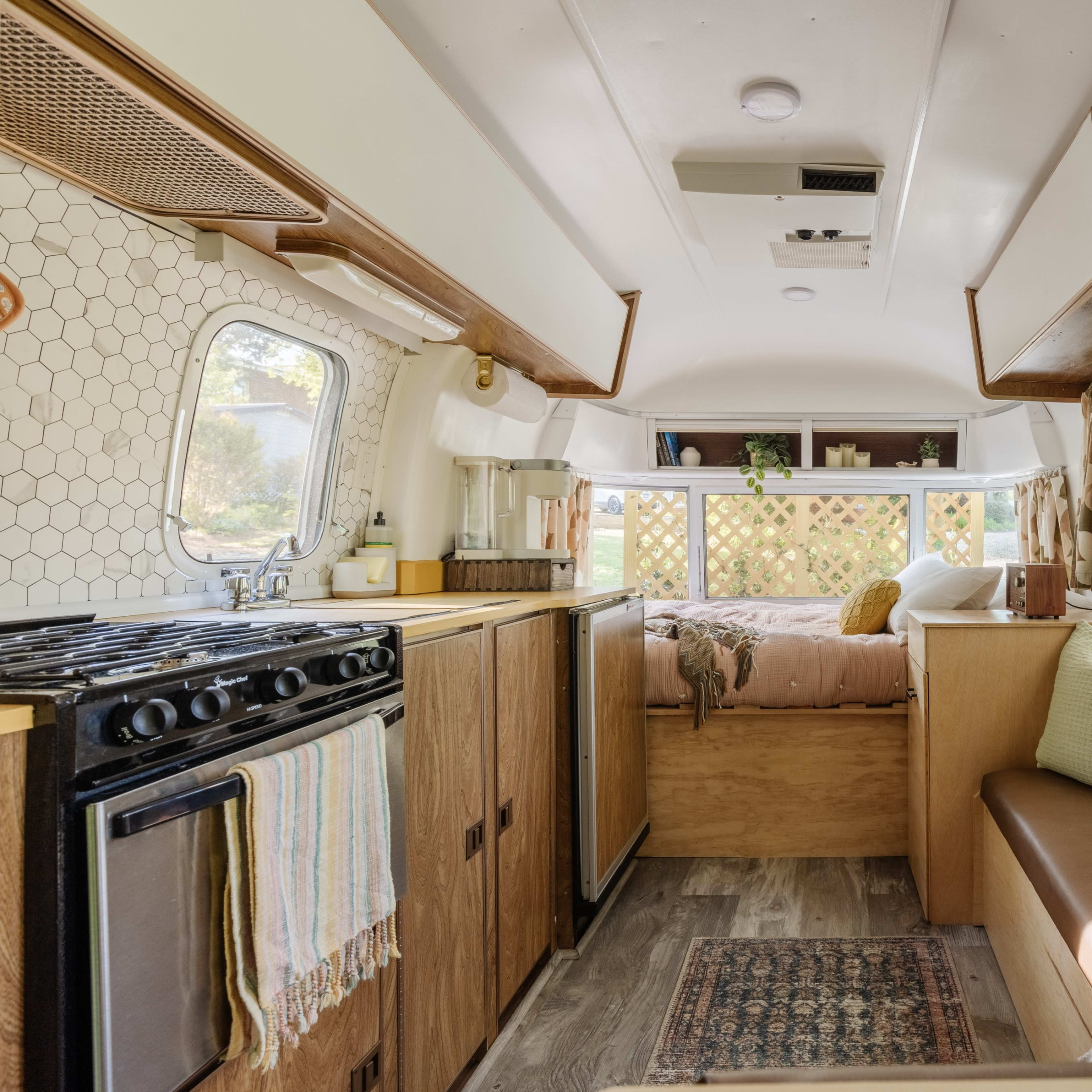 The interior of a recreational vehicle, featuring a kitchen area with a gas stove, a seating area, and large windows that let in natural light.
