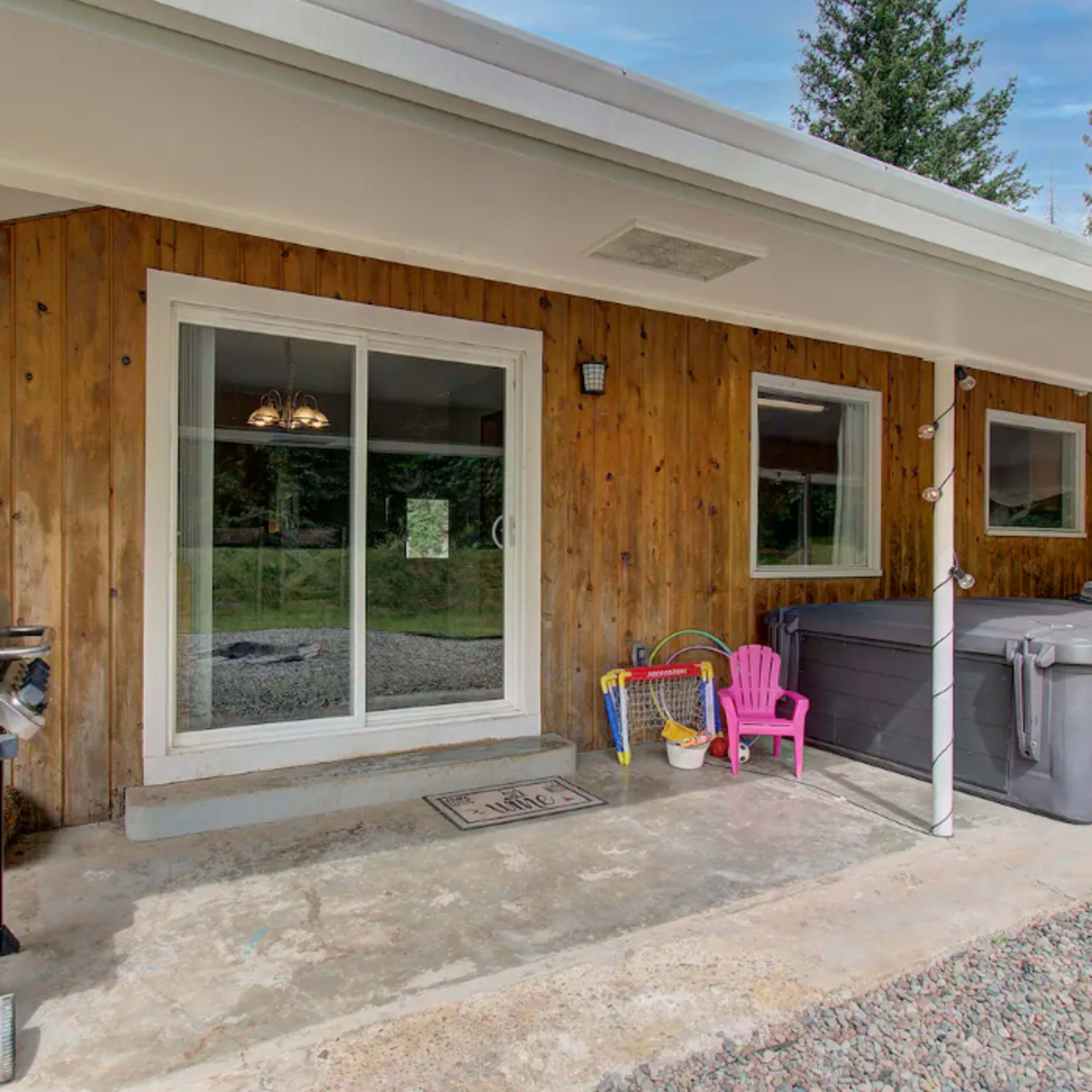 A patio area with a wooden wall, a sliding glass door, a grill, and a hot tub.