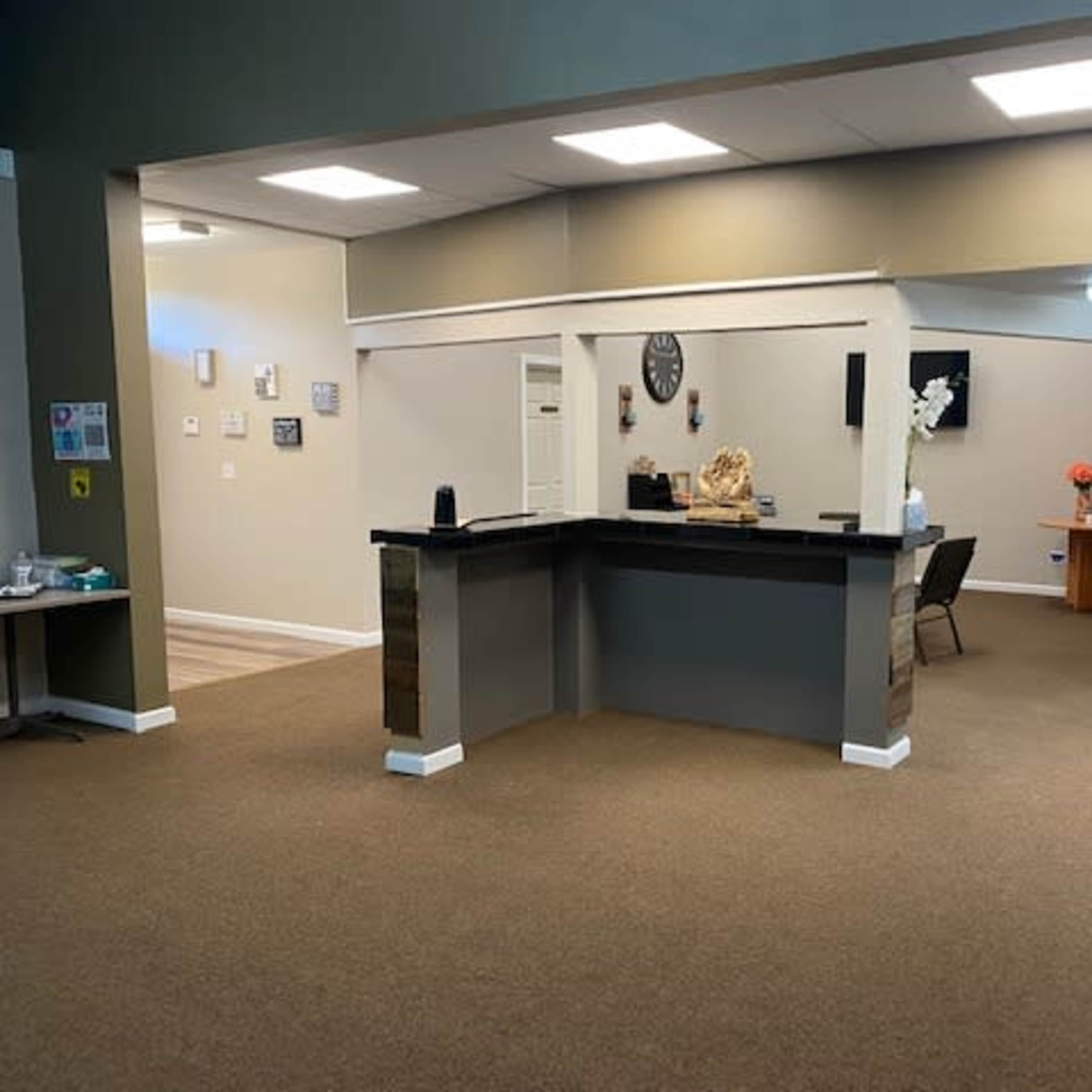 A spacious reception area with a dark countertop and light-colored walls, featuring a waiting area and an adjoining room.