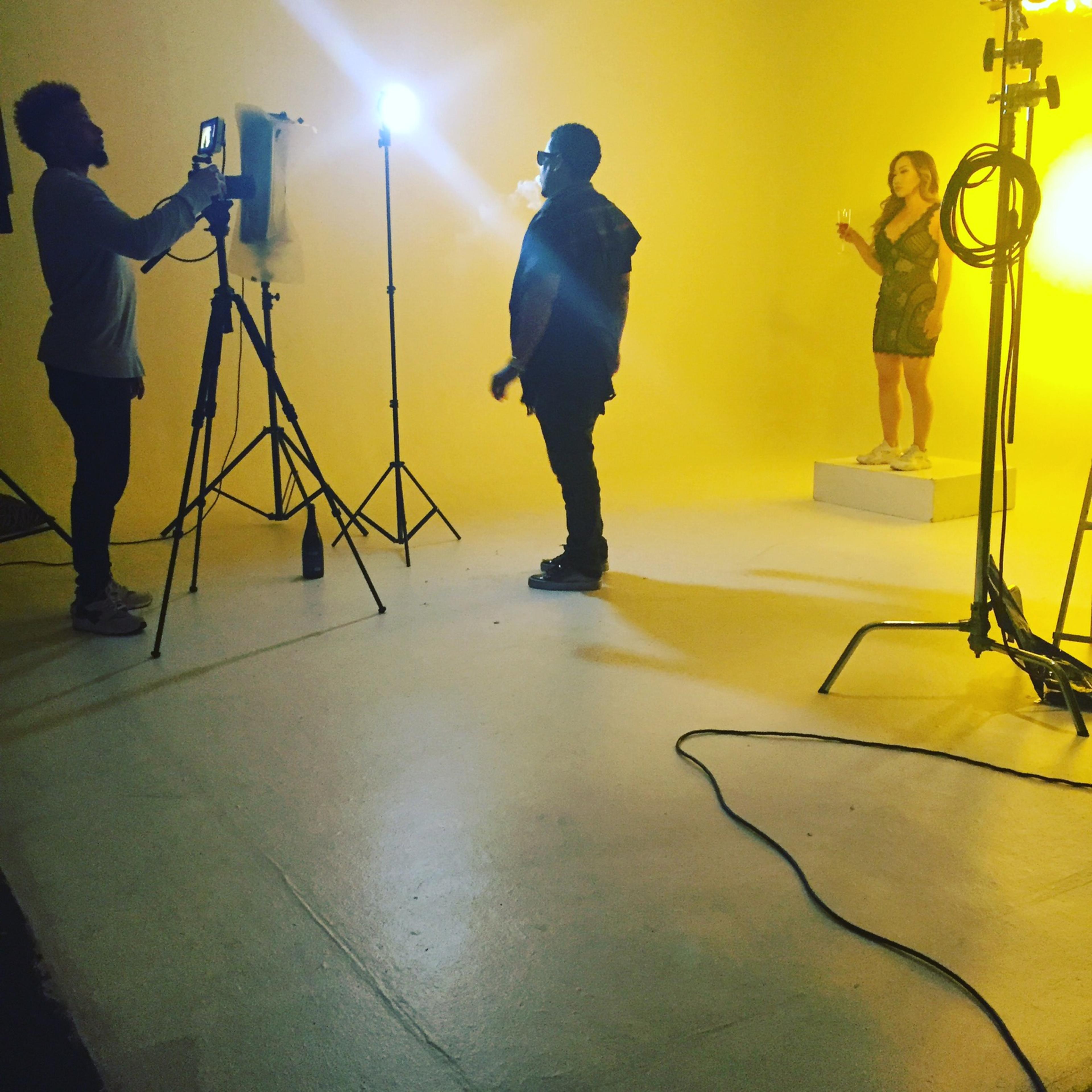 A photographer captures an image of a woman holding a drink on a pedestal, with studio lights illuminating the scene.