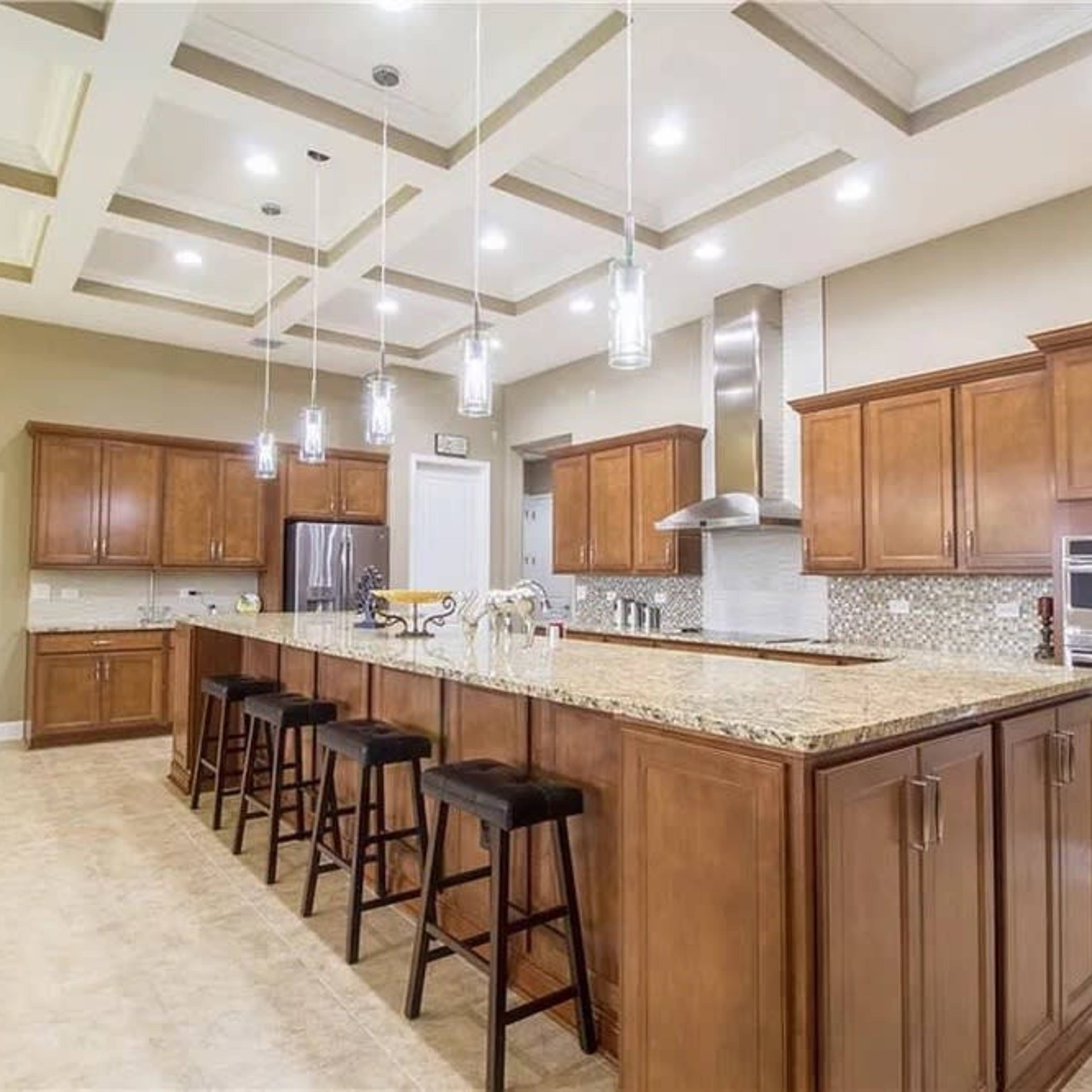 A spacious modern kitchen with wooden cabinetry, a large island with bar stools, and pendant lighting.