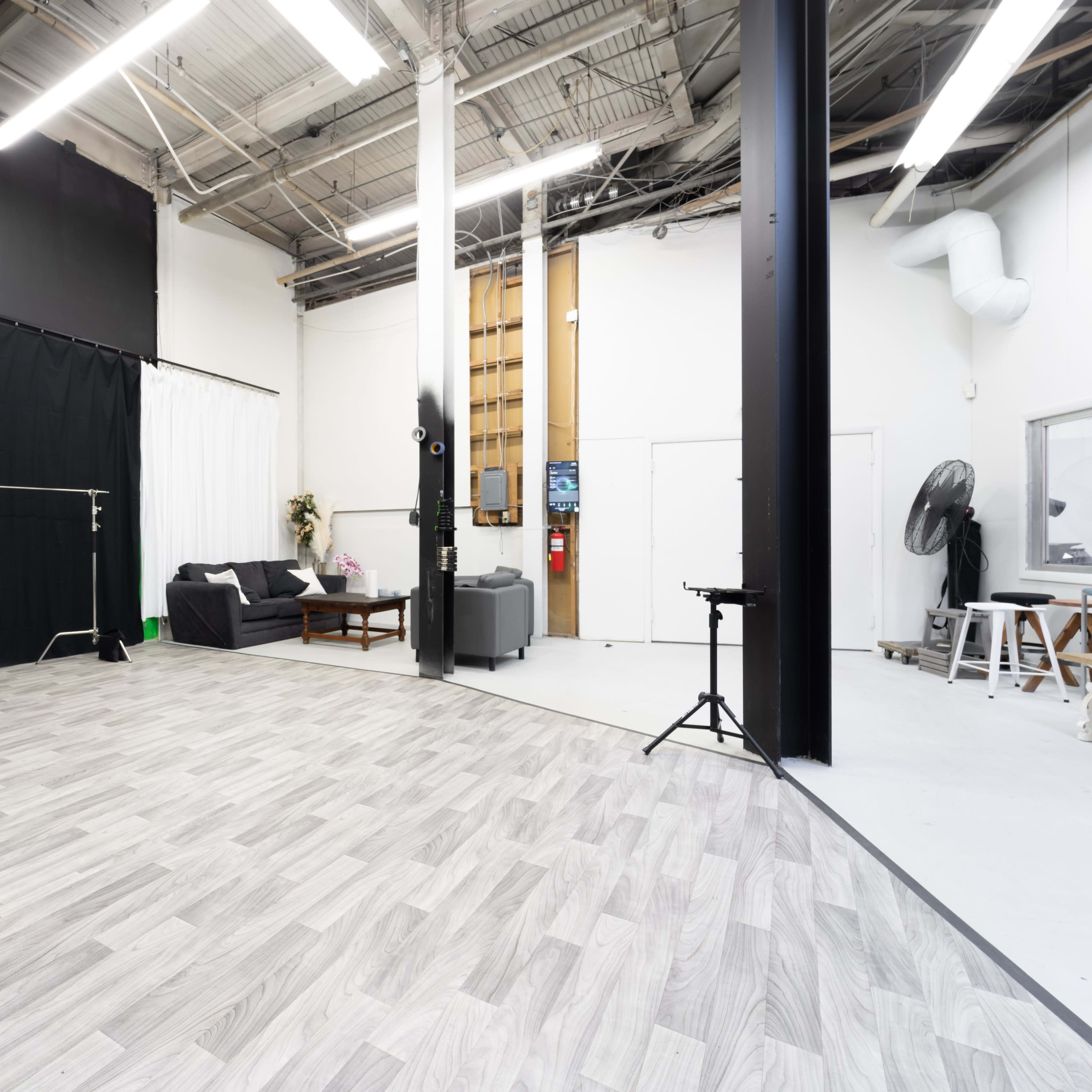A spacious studio with hardwood floors, black curtains, and seating areas set against white walls.