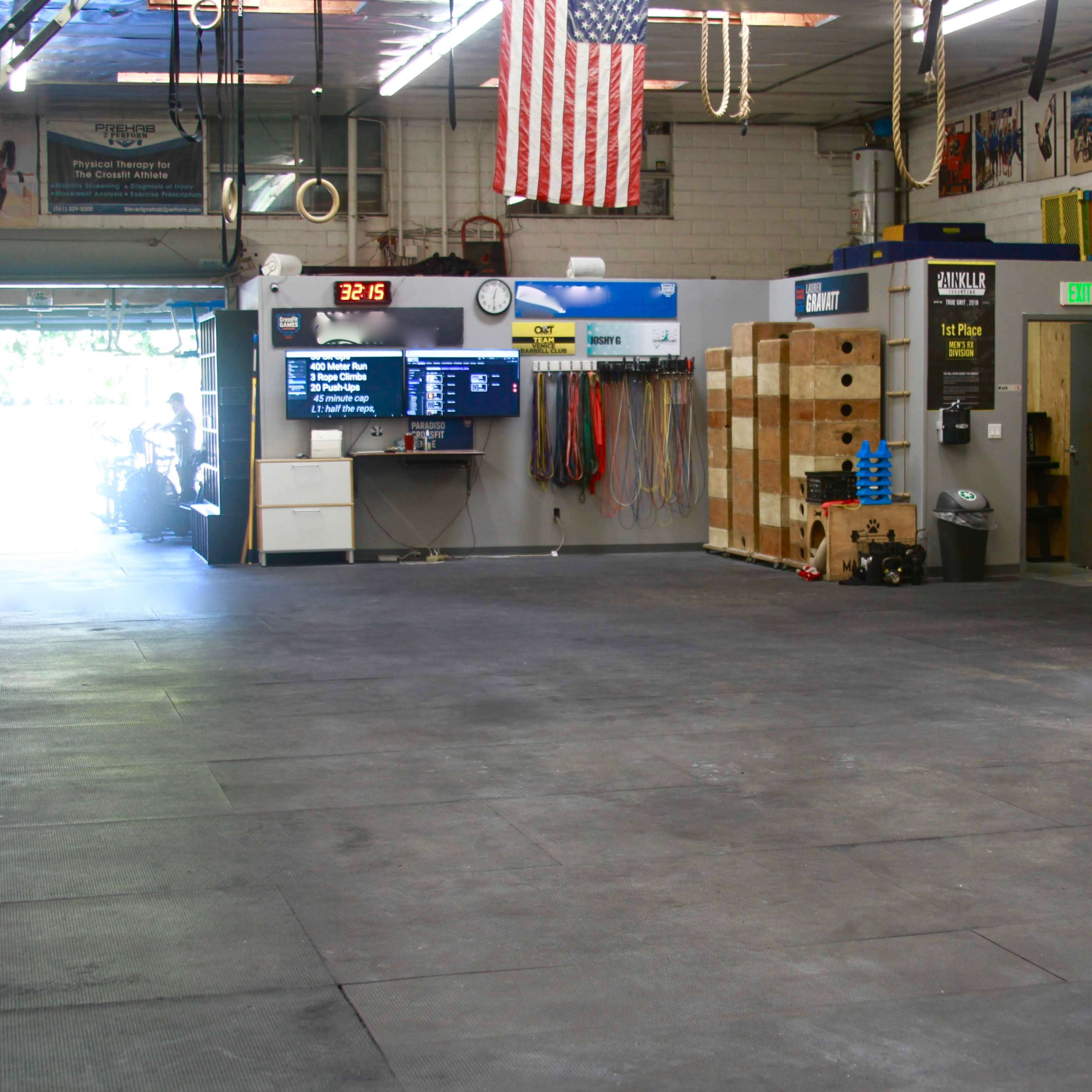 The interior of a gym with rubber flooring, exercise equipment, and an American flag hanging on the wall.
